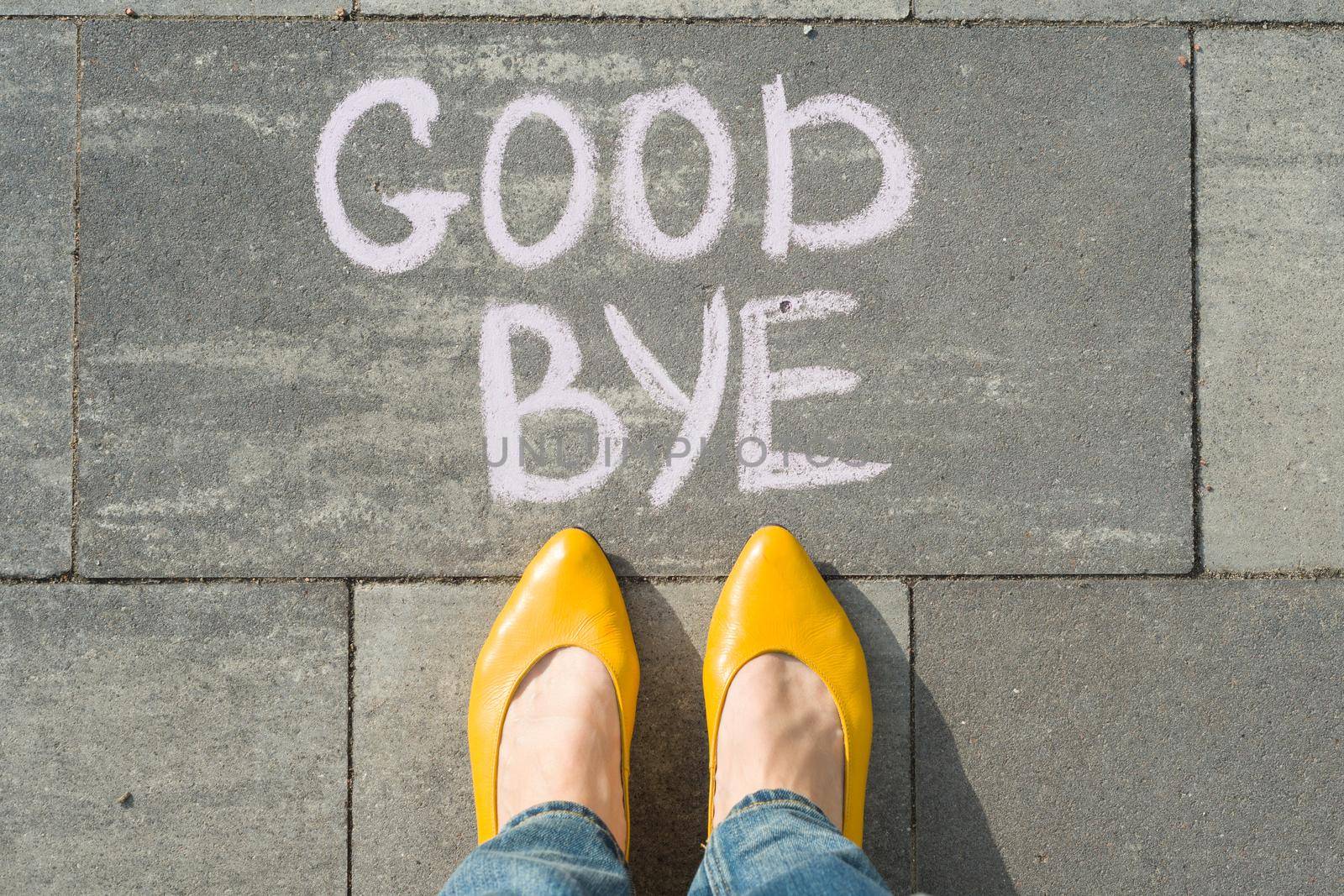 Female feet with text goodbye written on asphalt.