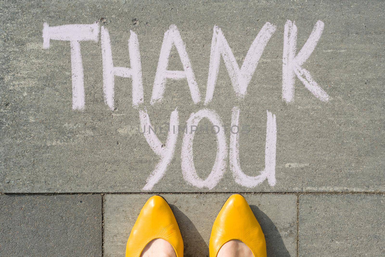 Female feet with text thank you written on grey sidewalk.