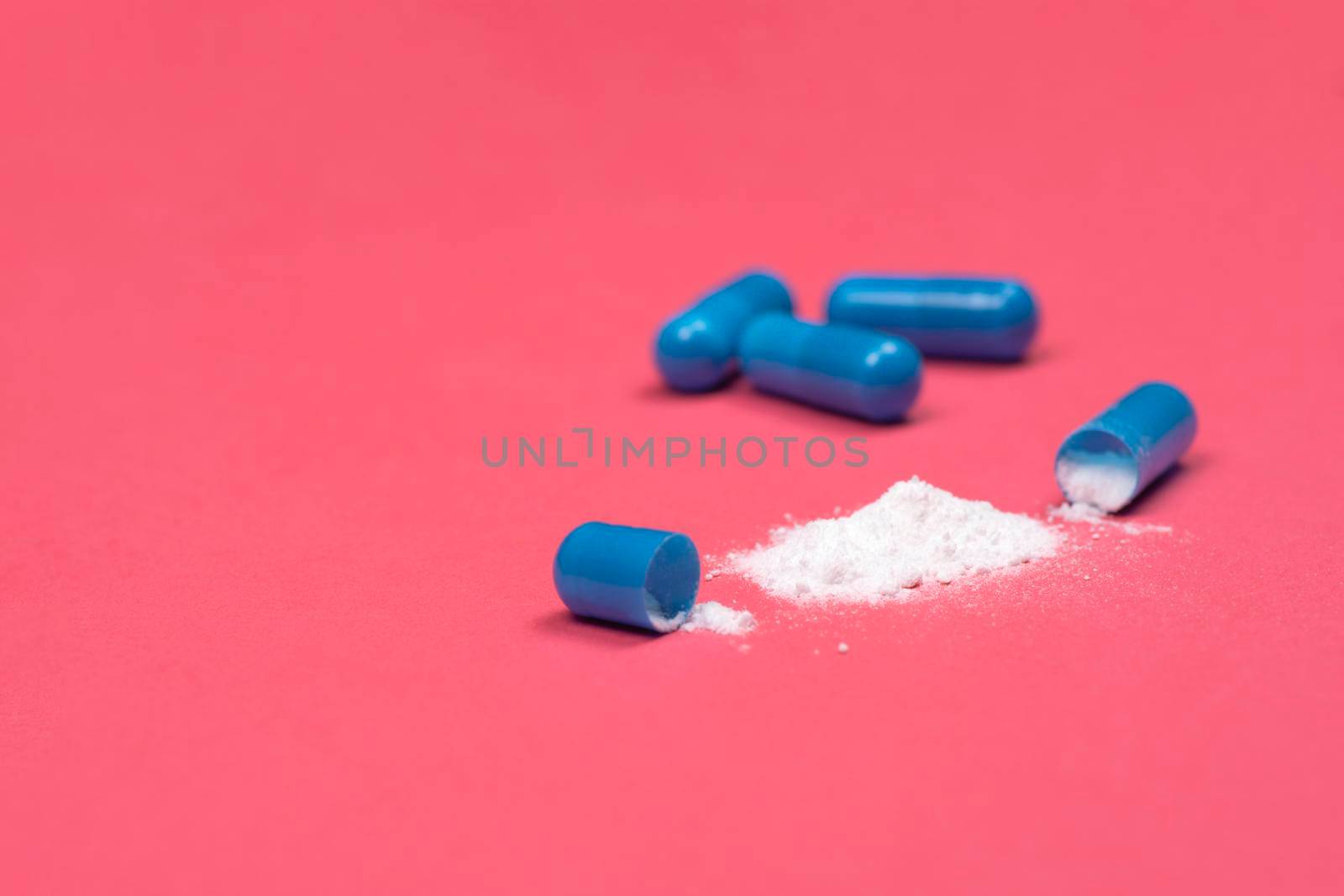 Medical background. Open blue capsule pill on pink background. Blue capsules pill spread on fuchsia or pink background with copy space. Macro photo