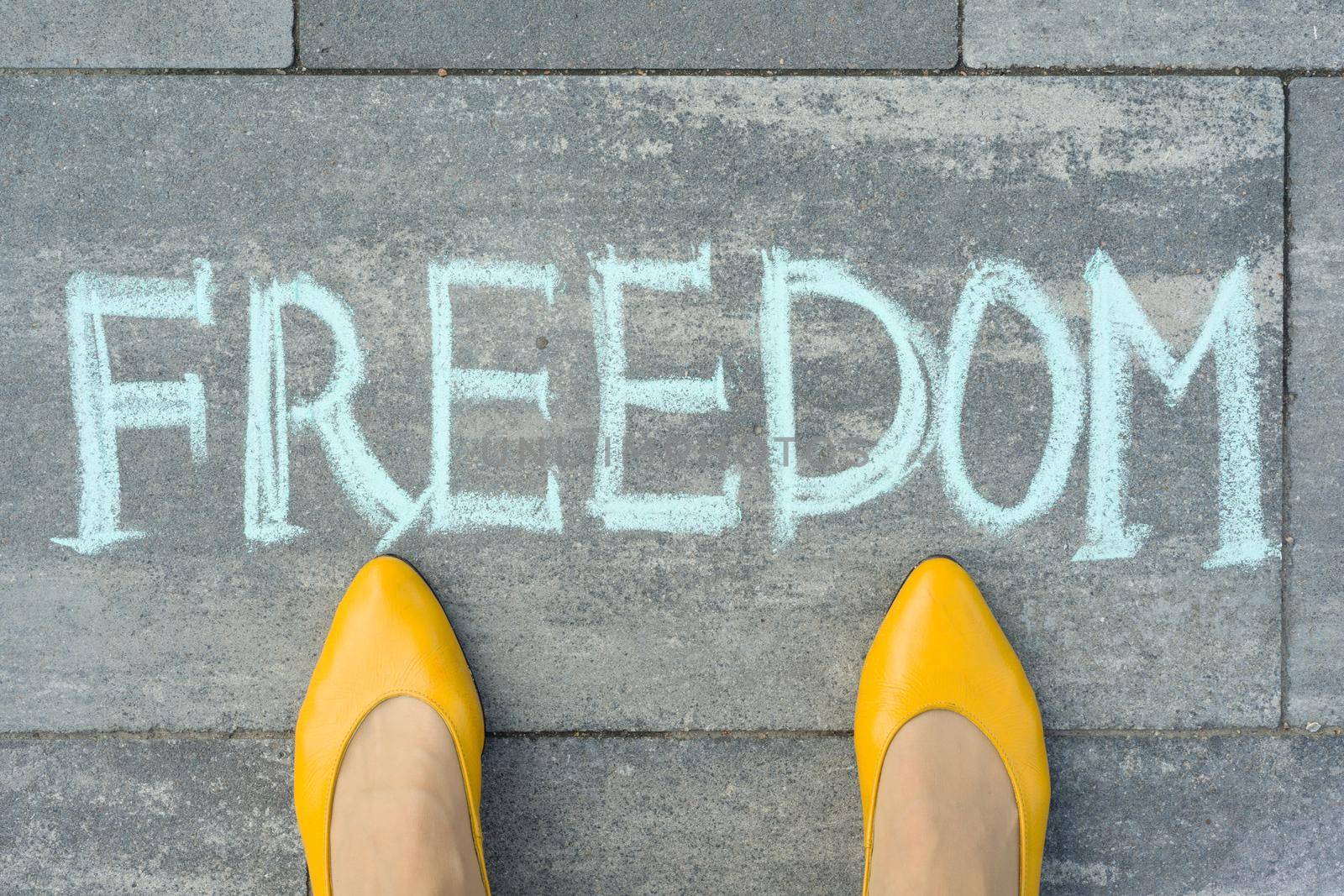 Female feet with text freedom written on grey sidewalk.