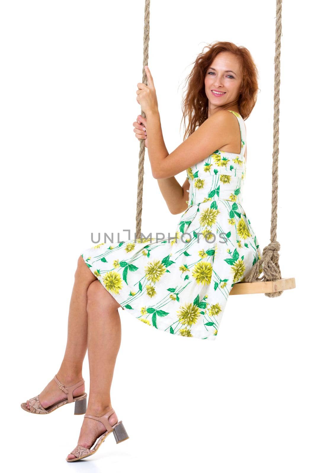 Beautiful young woman swinging on rope swing. Side view of happy woman wearing summer dress sitting on swing on isolated white background. Happy holidays and recreation concept