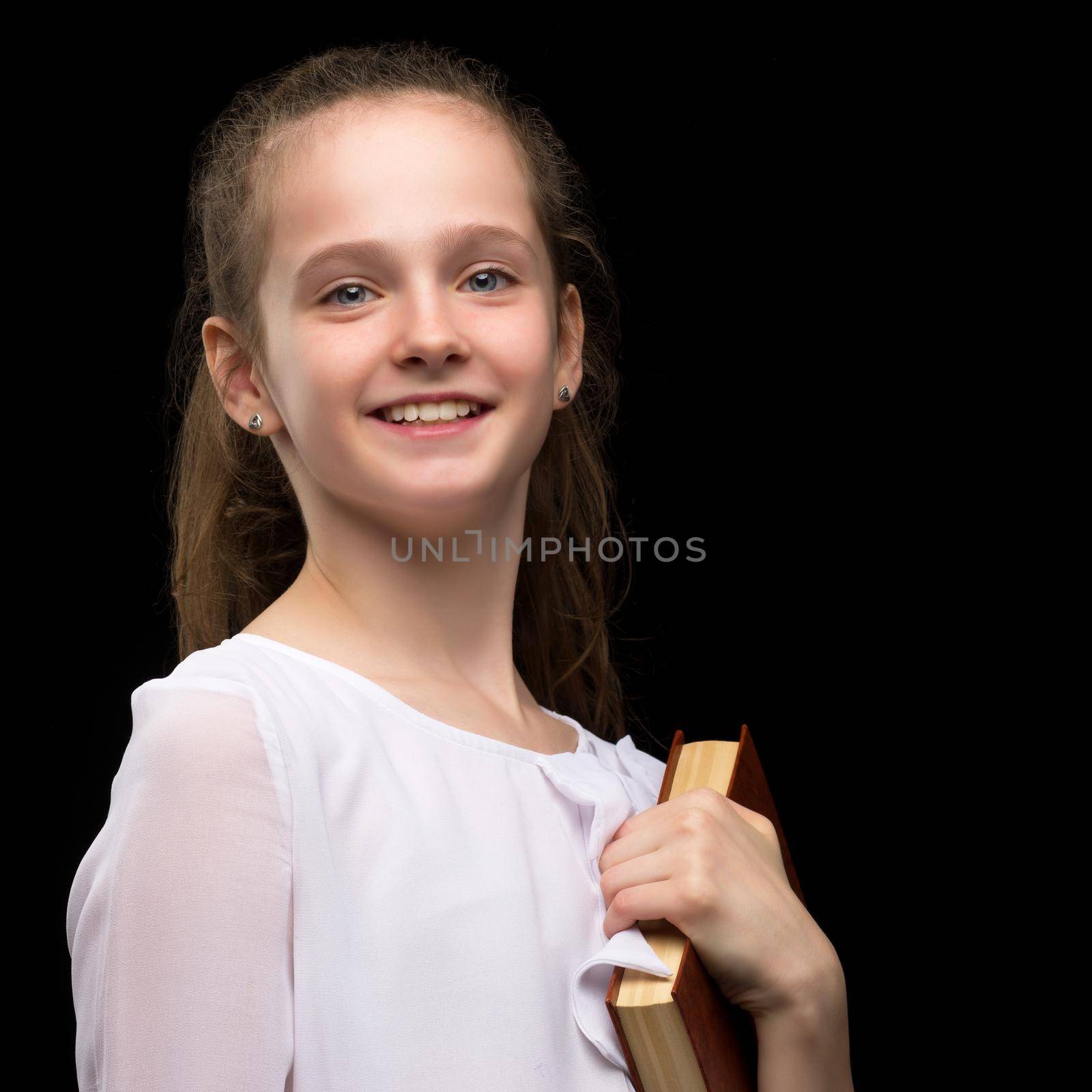 Beautiful little girl in a school uniform with a book on a black background. Literature and education concept, children's emotions.