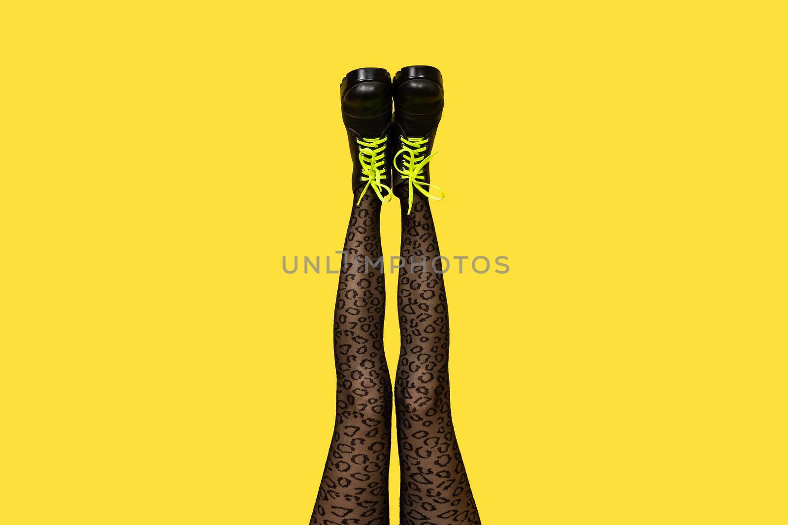 New gray female boots with bright yellow laces on straight, long slender woman legs in gray tiger print tights isolated on yellow background. Pop art concept banner with copy space.