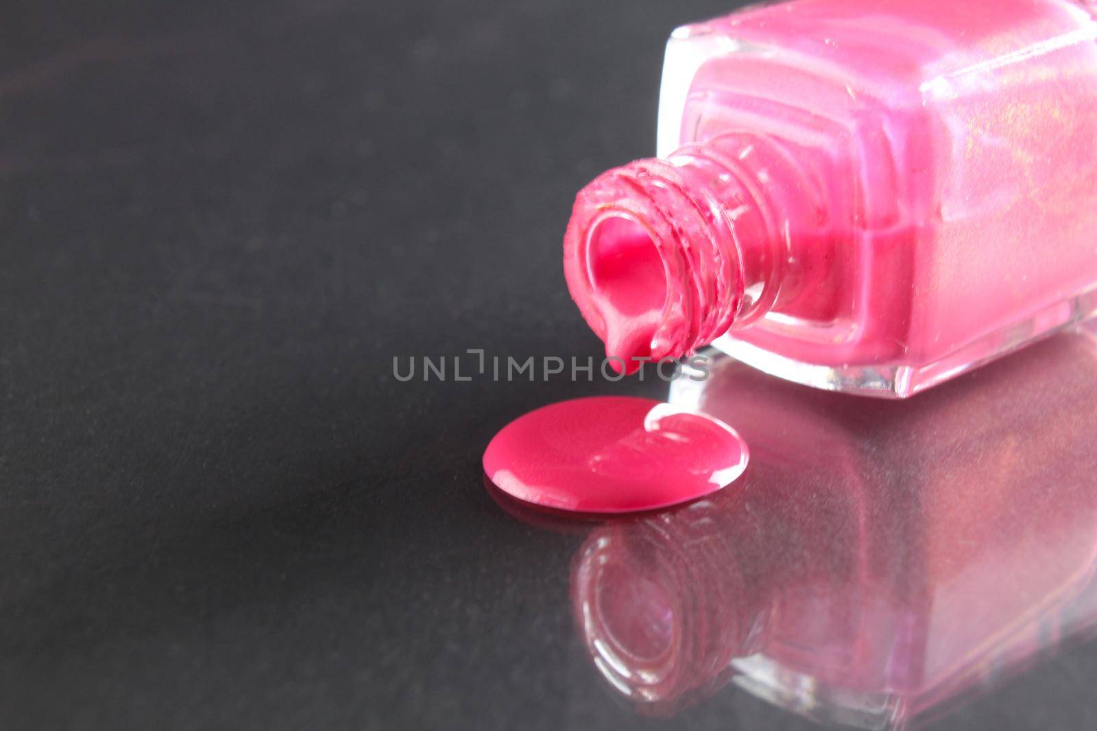 Pink nail polish is poured out of the bottle bottle on a black background with a copyspace place for text.