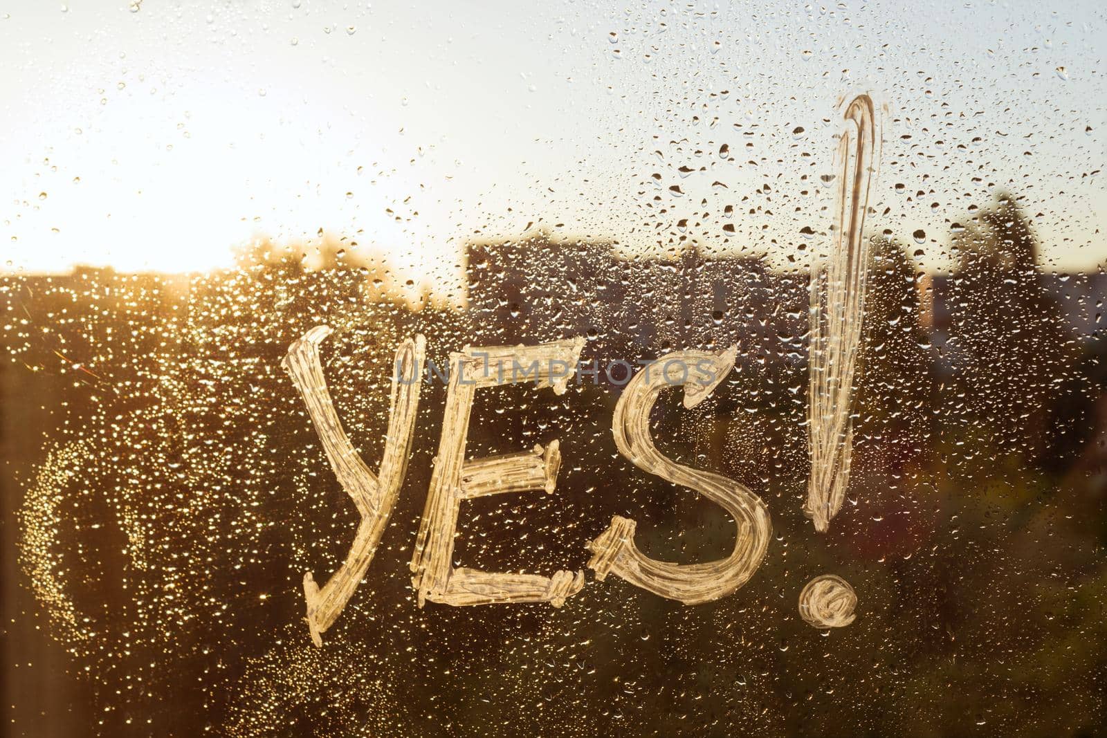 The word yes on the window with water drops on sunny background, yes written with white toothpaste.