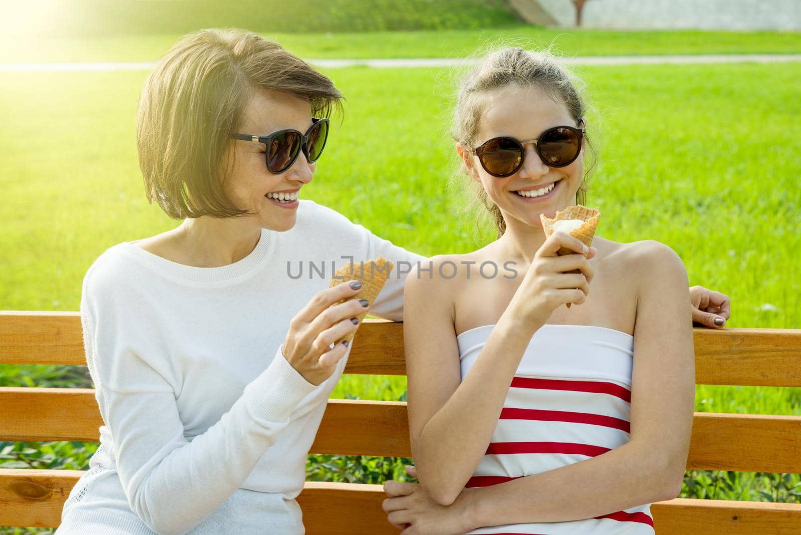 Holiday with the family. Happy young mother and cute daughter of a teenager in a city park eating ice cream, talking and laughing