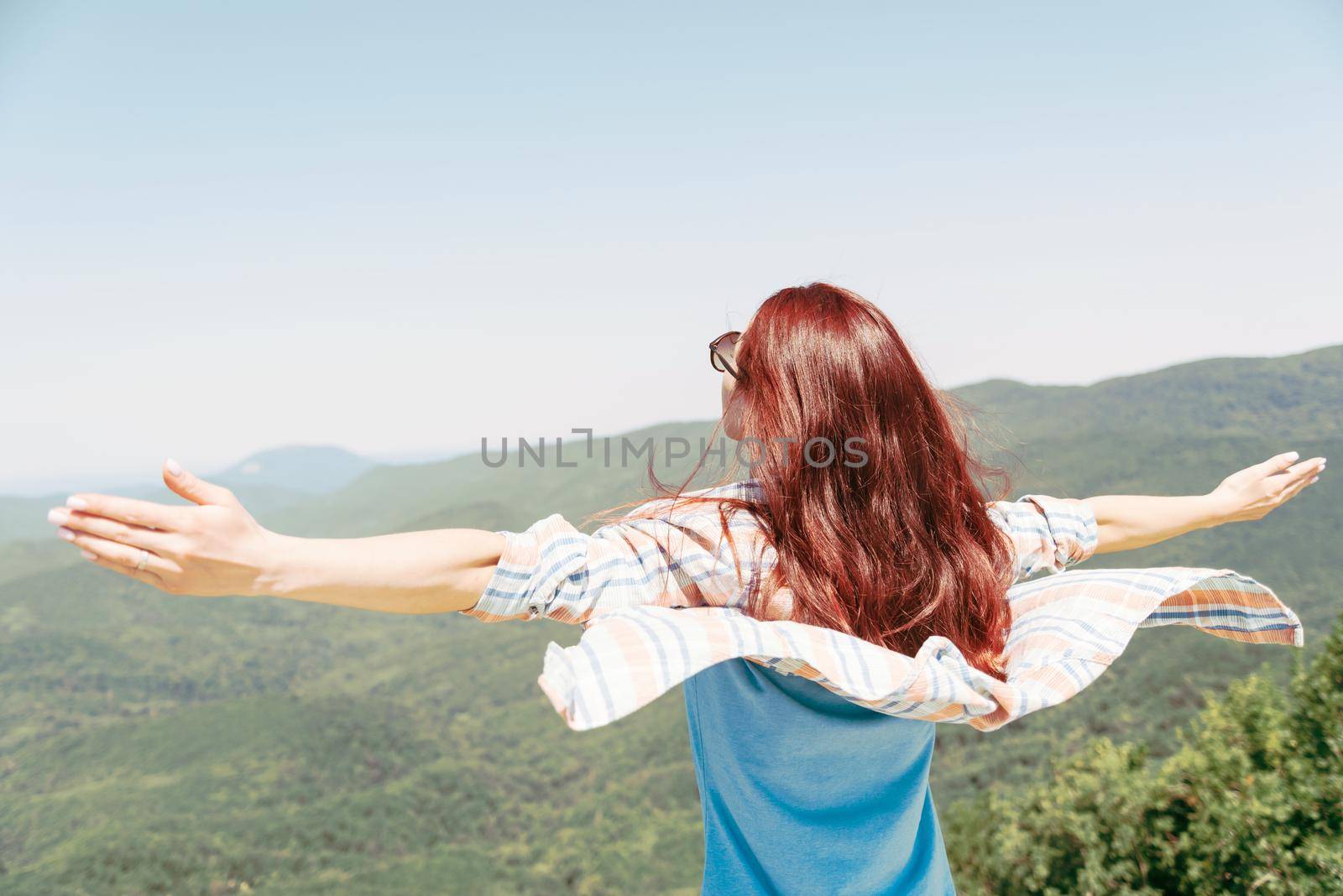 Freedom happy young woman standing with raised arm in windy weather high in the summer mountains.