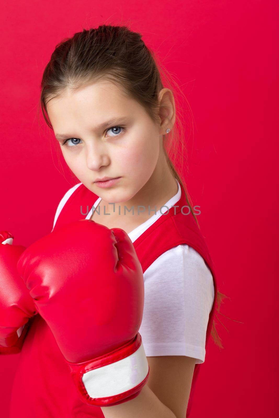Teenage girl posing in boxing gloves. Portrait of sportive boxer girl dressed sportswear ready to fight. Child training on red background. Healthy lifestyle, sport and fitness concept