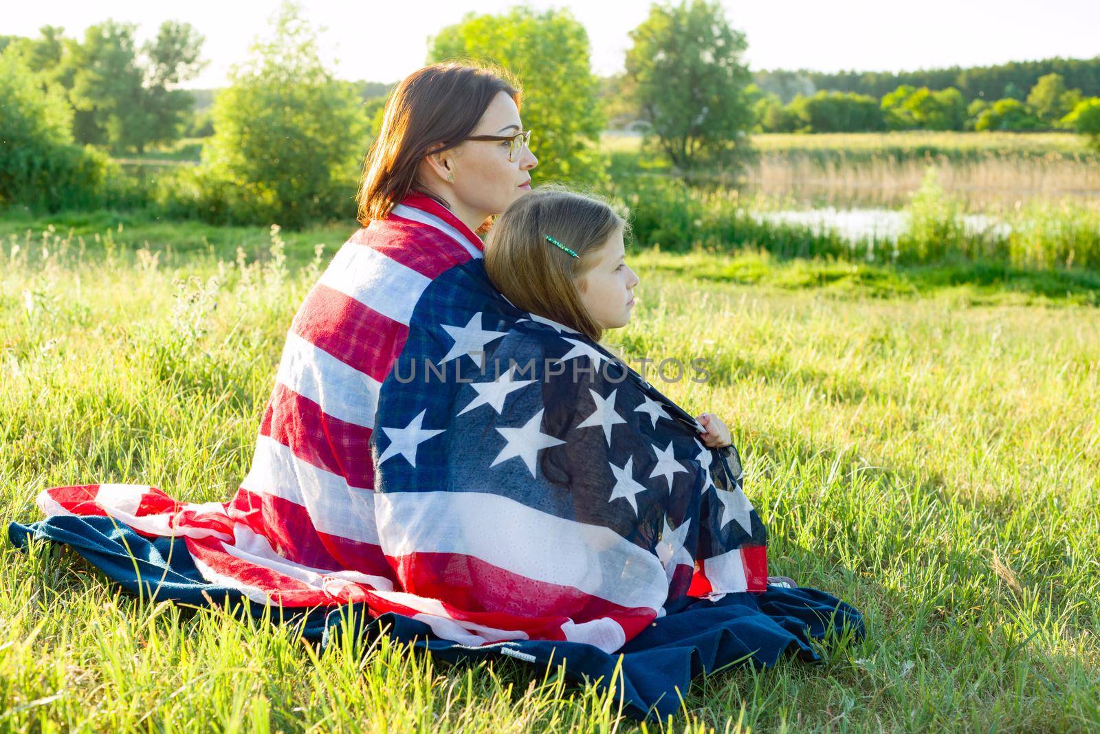 Portrait of mother and daughter with American flag. Look at the natural rural landscape,view from the back.