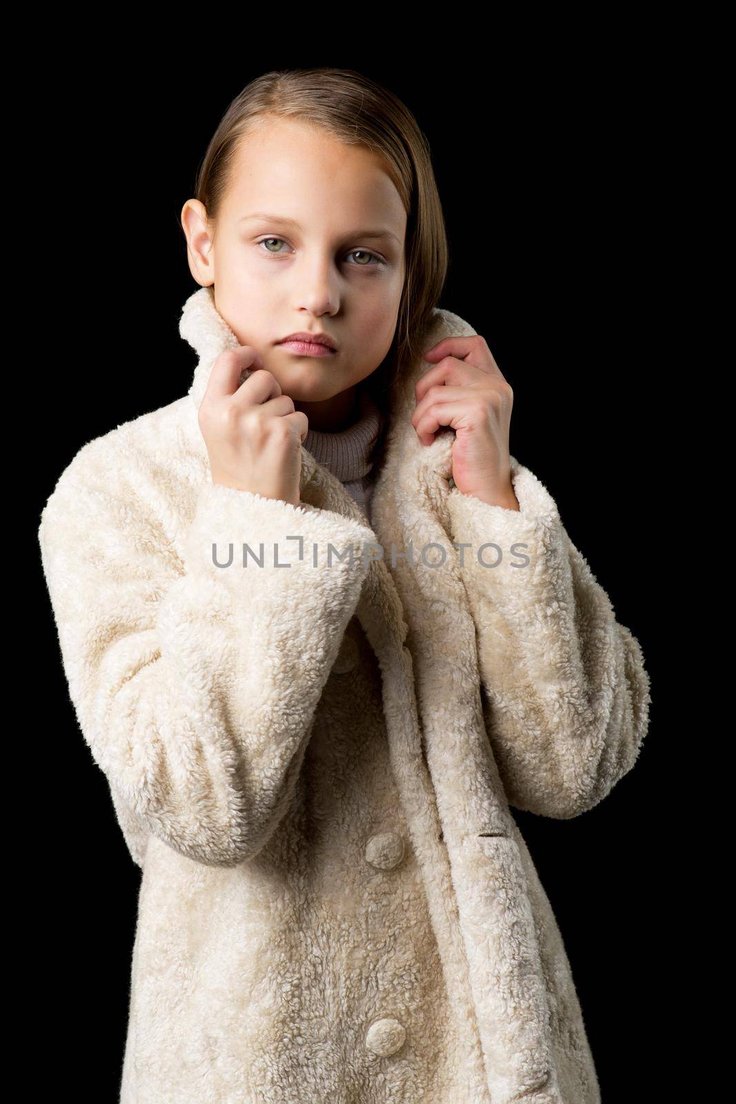 Pretty girl in fashionable outfit. Stylish beautiful girl wearing beige fur coat and jeans. Full length portrait of preteen child posing in studio against black background