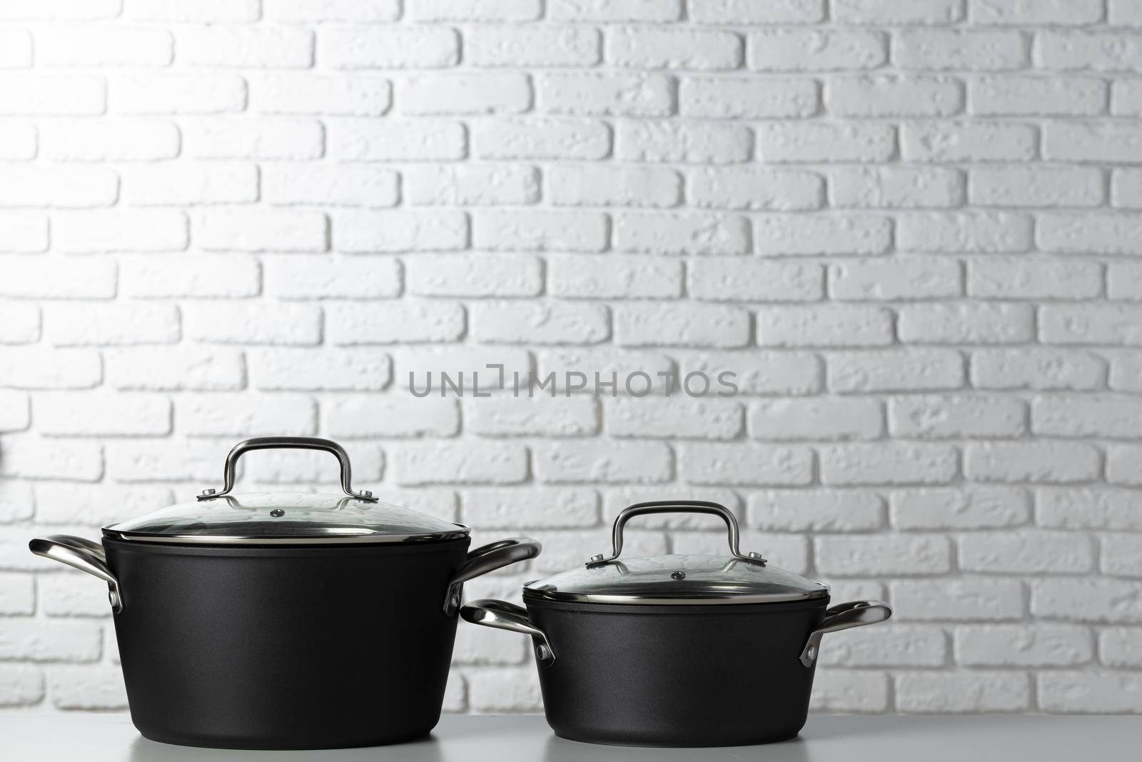 Black kitchenware on table against white brick wall, front view