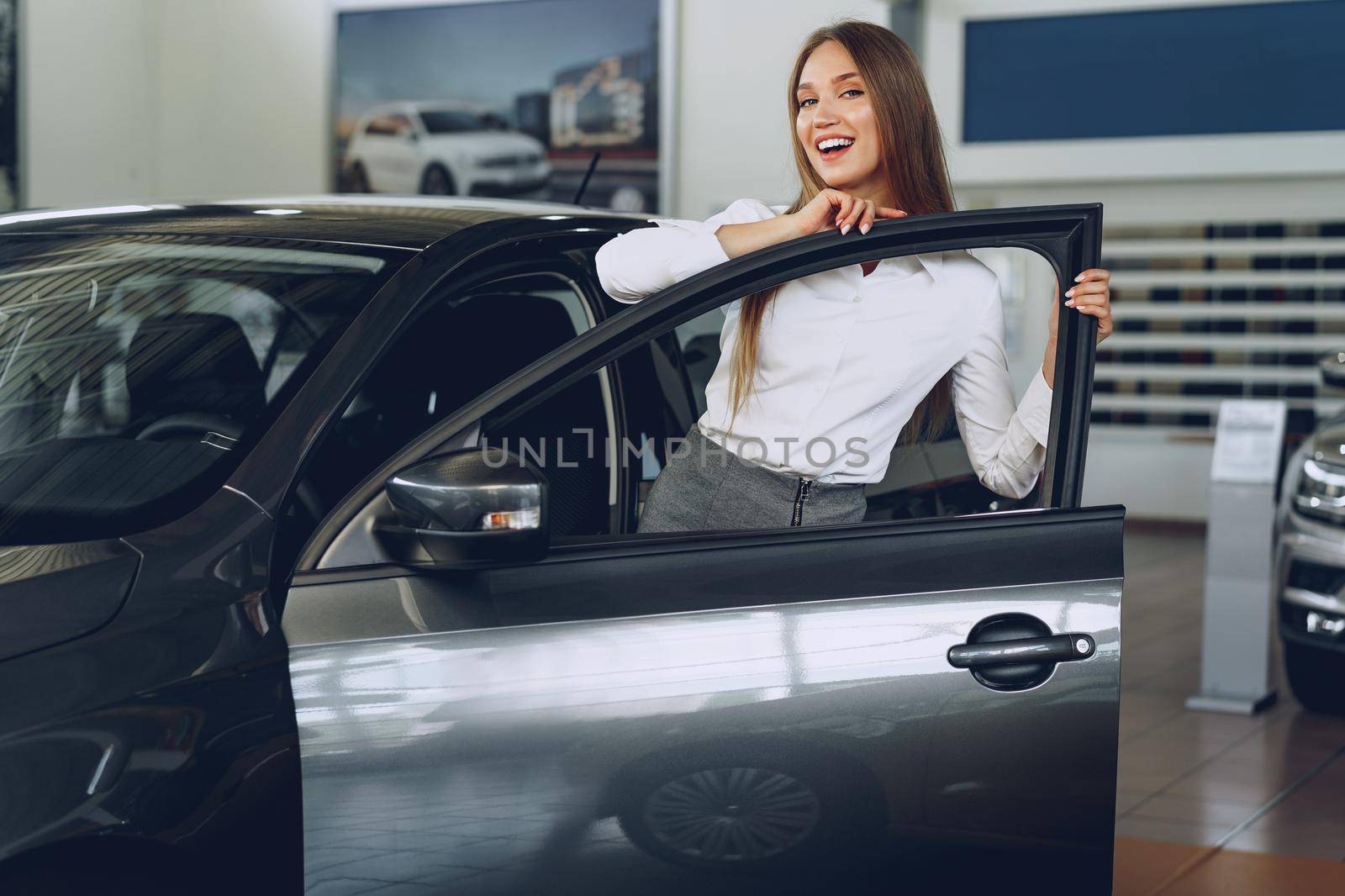 Beautiful young woman touching her new car with pleasure by Fabrikasimf