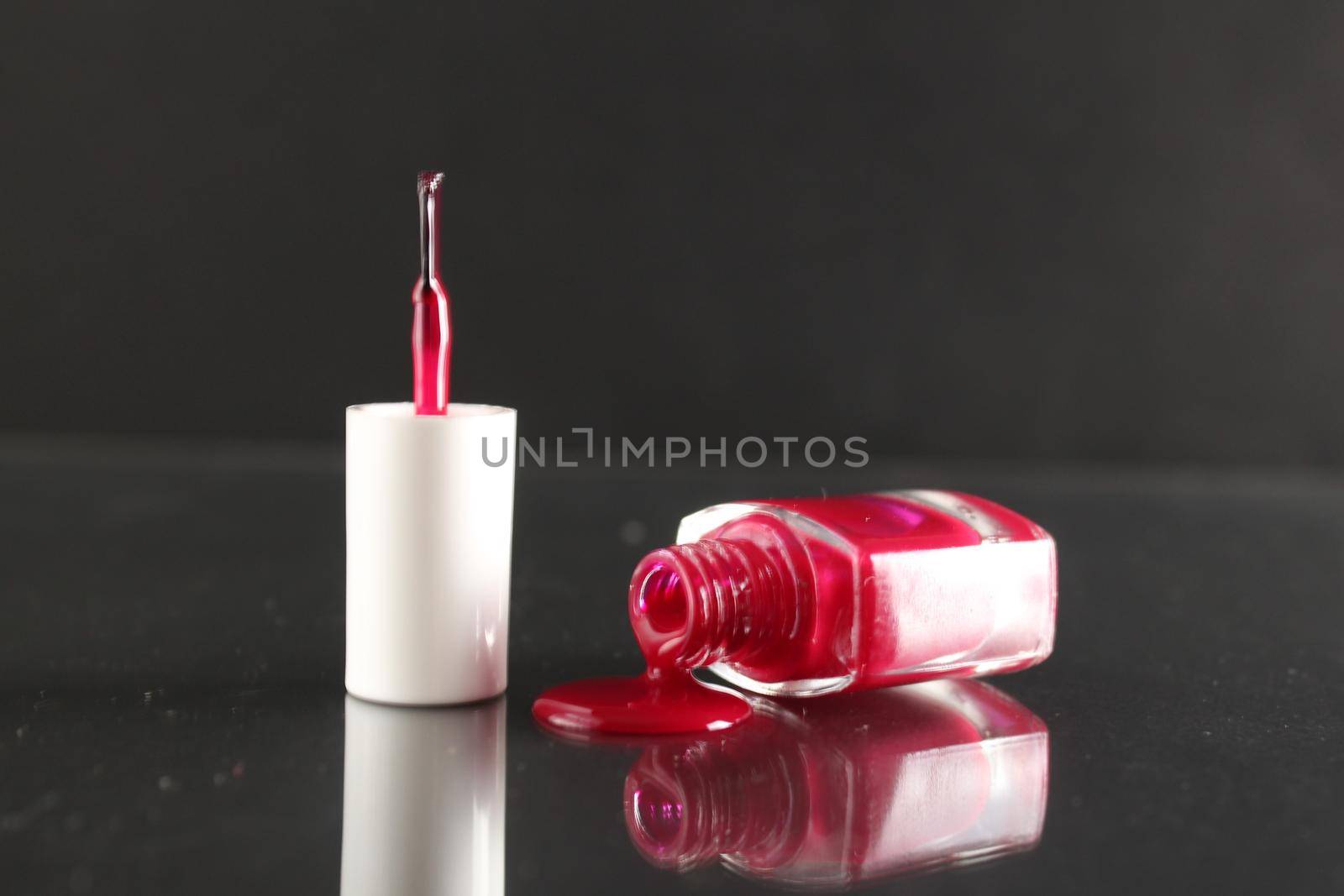 Burgundy red lacquer for leggings flows from the bottle of the bottle close-up view from the side on a black background with a copyspace.