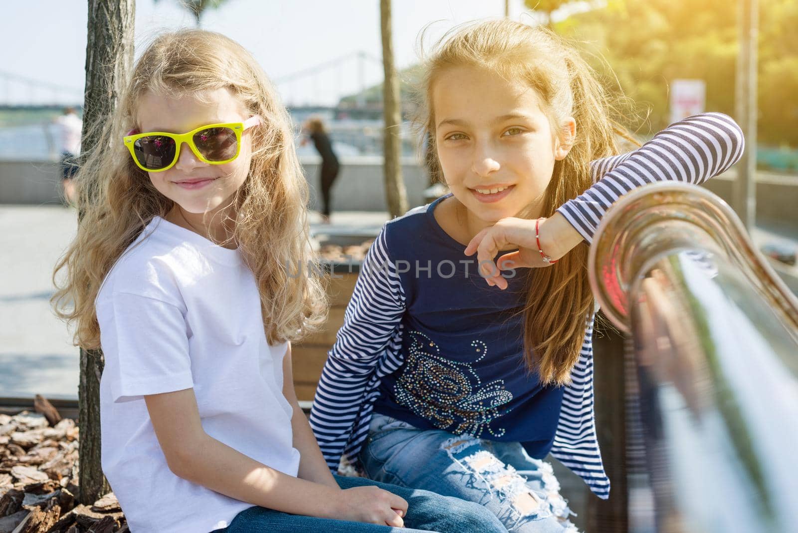 Two pretty little girls are looking at the camera and smiling. Background urban, summer, embankment of the river by VH-studio