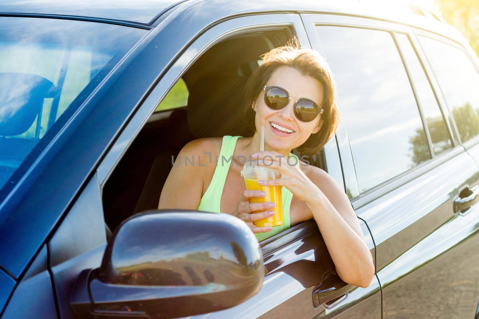 Beautiful female driver smiling while driving his car, drinking orange juice