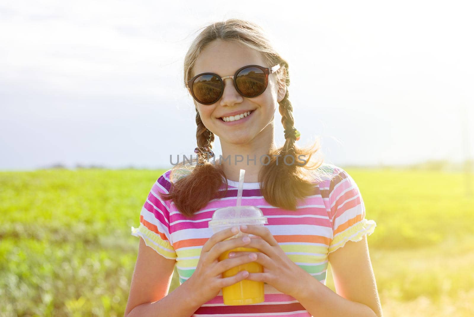 Happy girl drinking orange juice at hot summer day. Outdoor