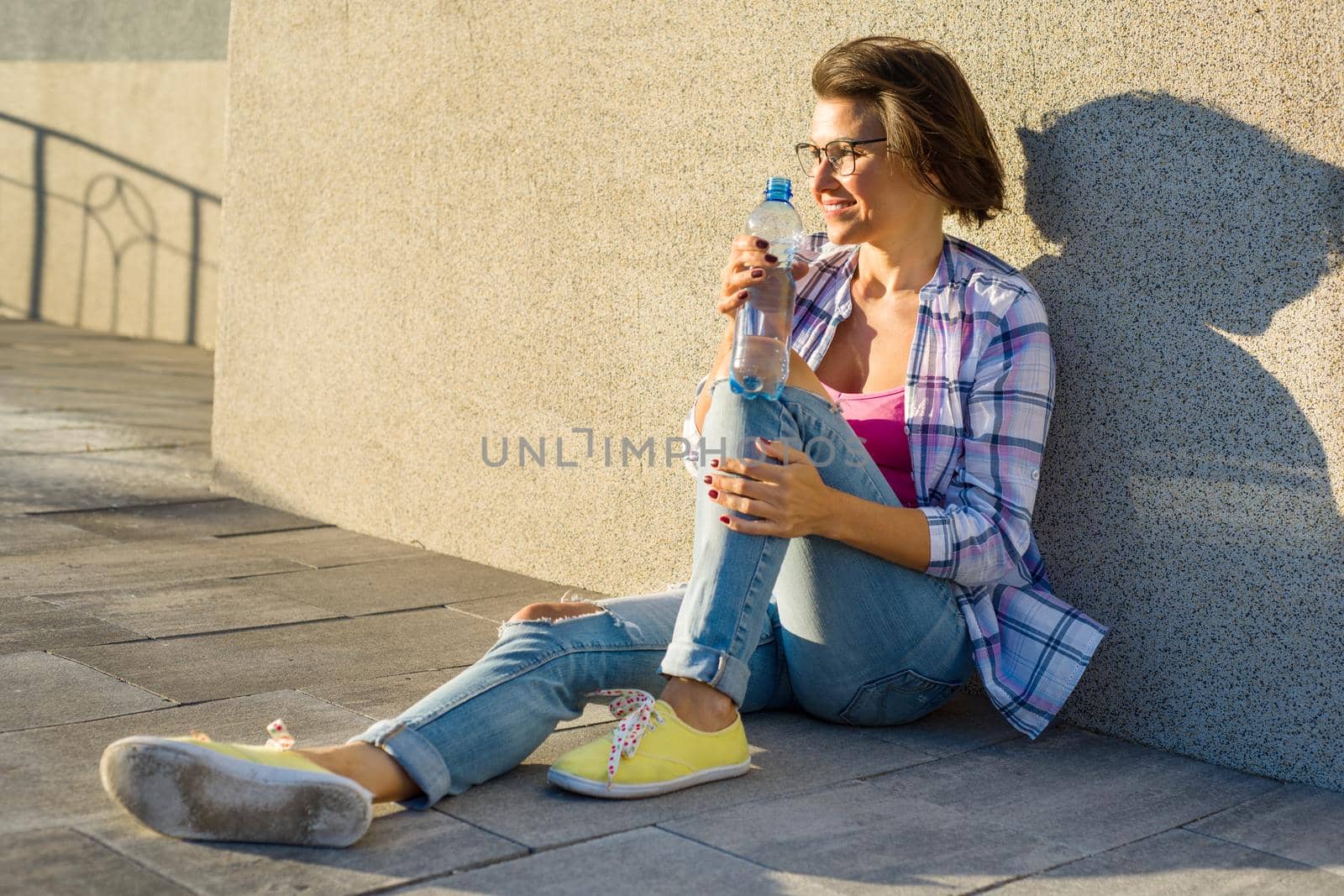 Adult healthy woman drinks water from bottle. Outdoor portrait