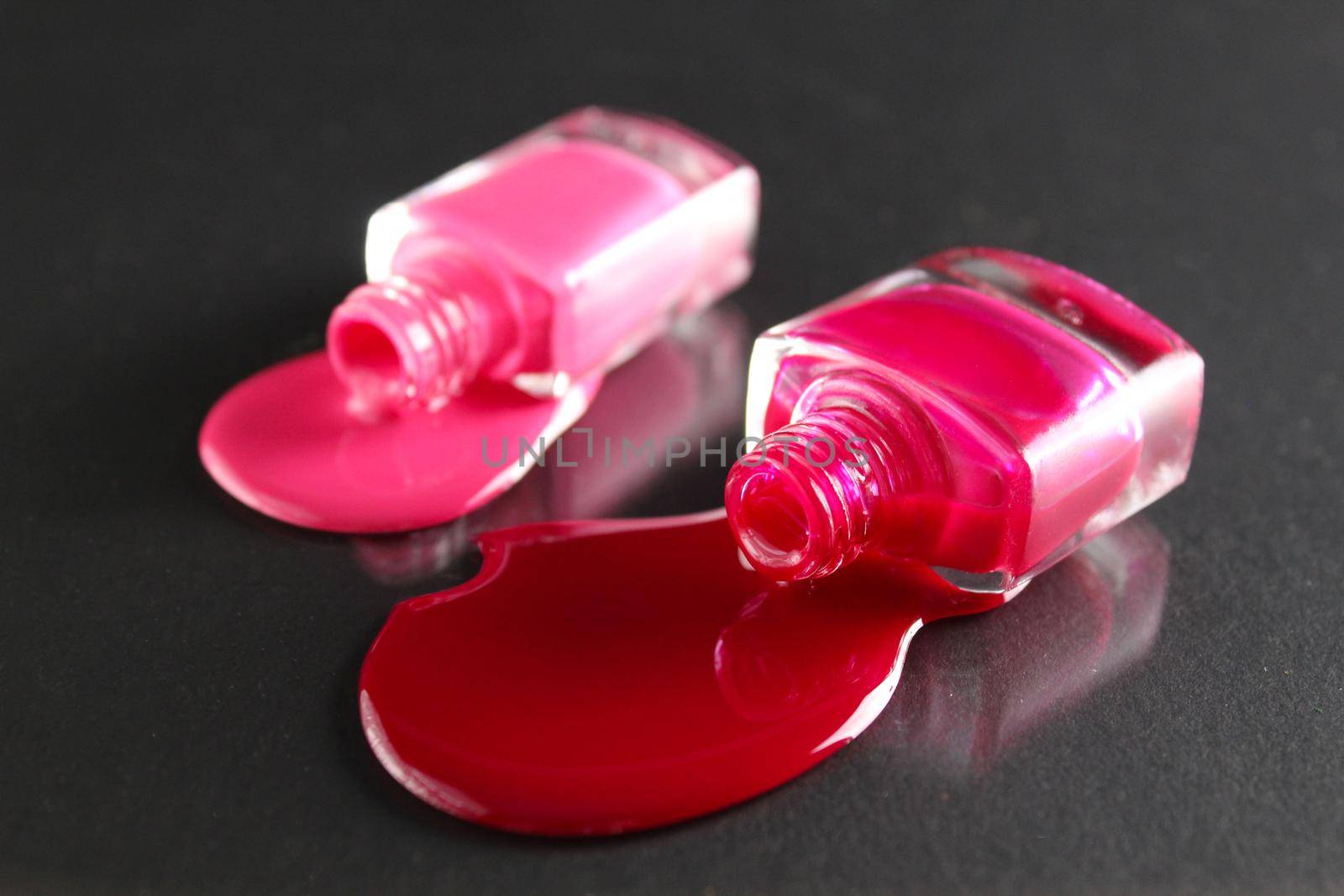 Beauty background two bottles of nail polish bottles red or burgundy pink spill poured on the table on a black background with a copyspace .