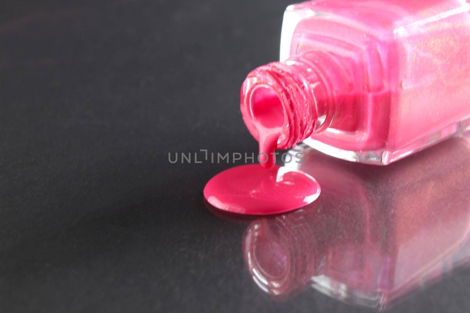 Pink nail polish is poured out of the bottle bottle on a black background with a copyspace place for text by Shoba