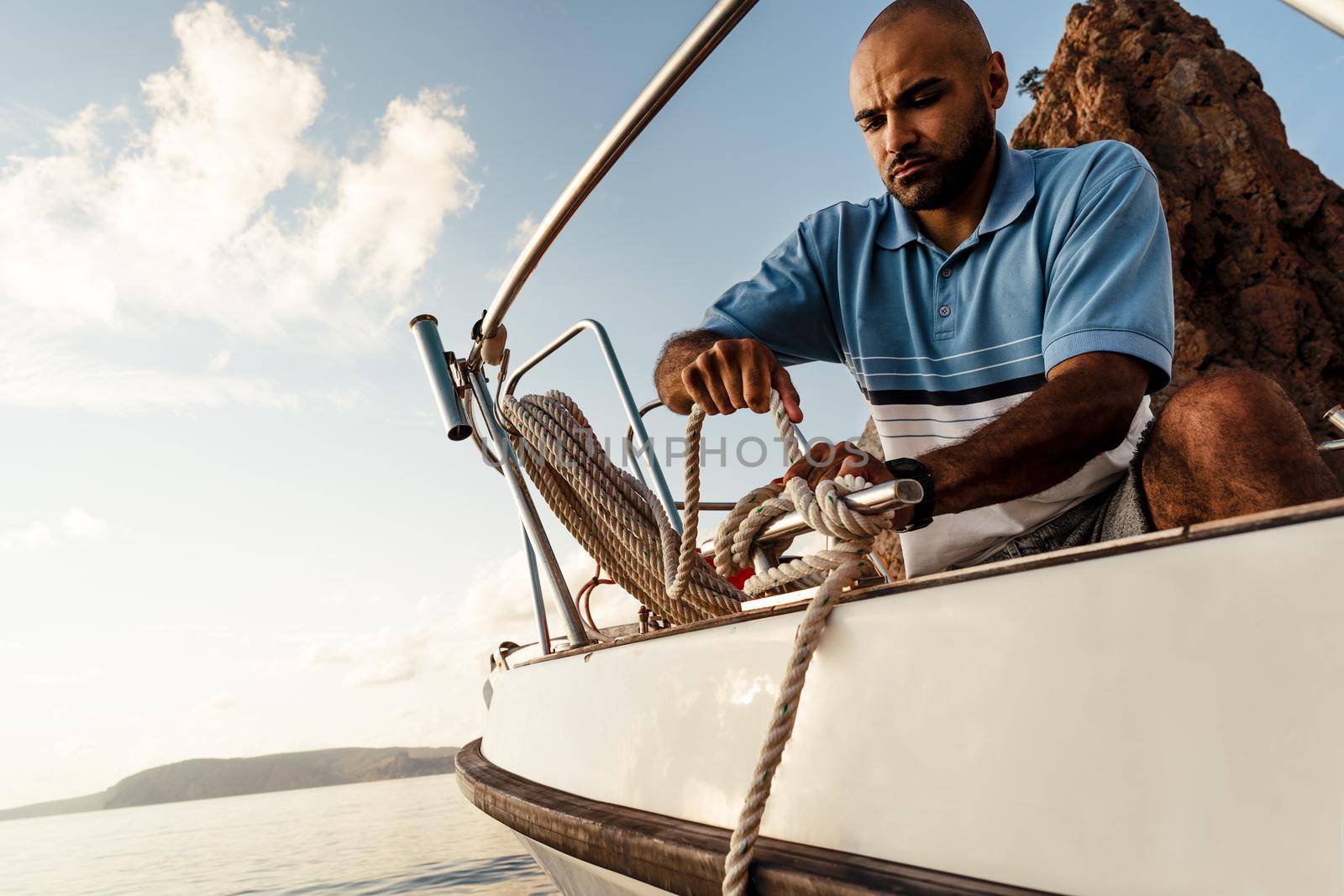 Young african american sailor tying ropes on sailboat in the sea on sunset, close up