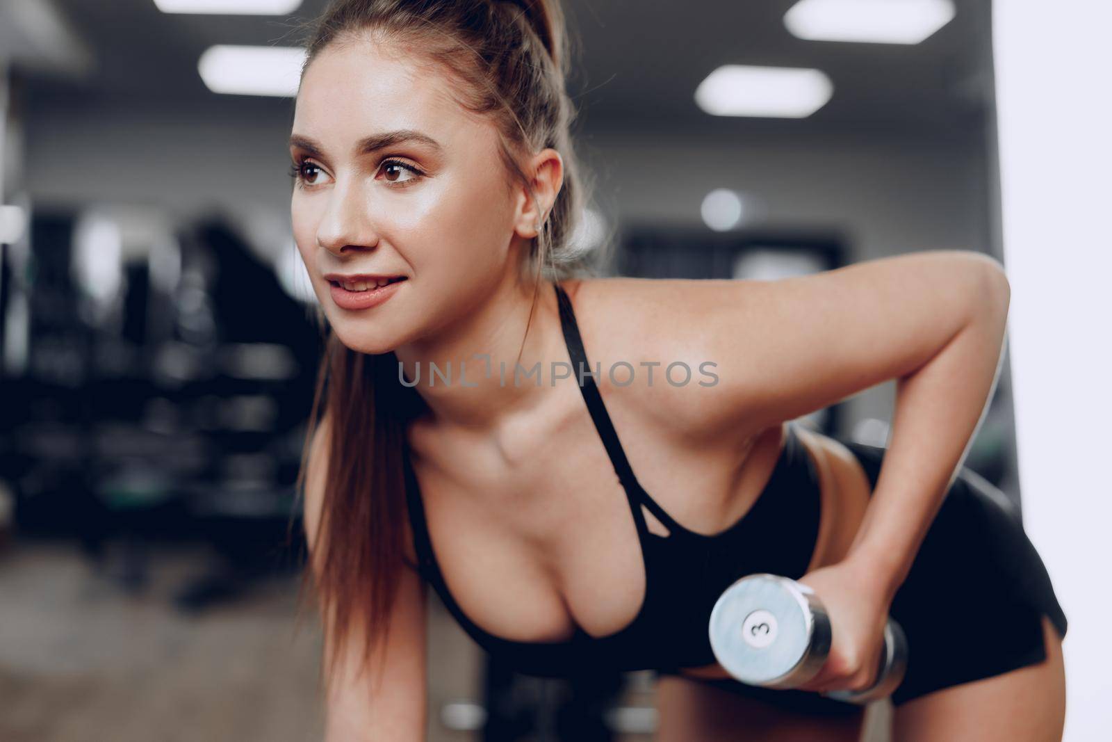 Young brunette sporty woman exercising with dumbbell in a gym close up