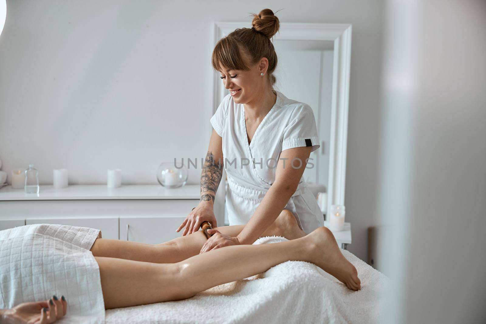 Conident female specialist is doing leg massage with bamboo stick to beautiful caucasean woman client