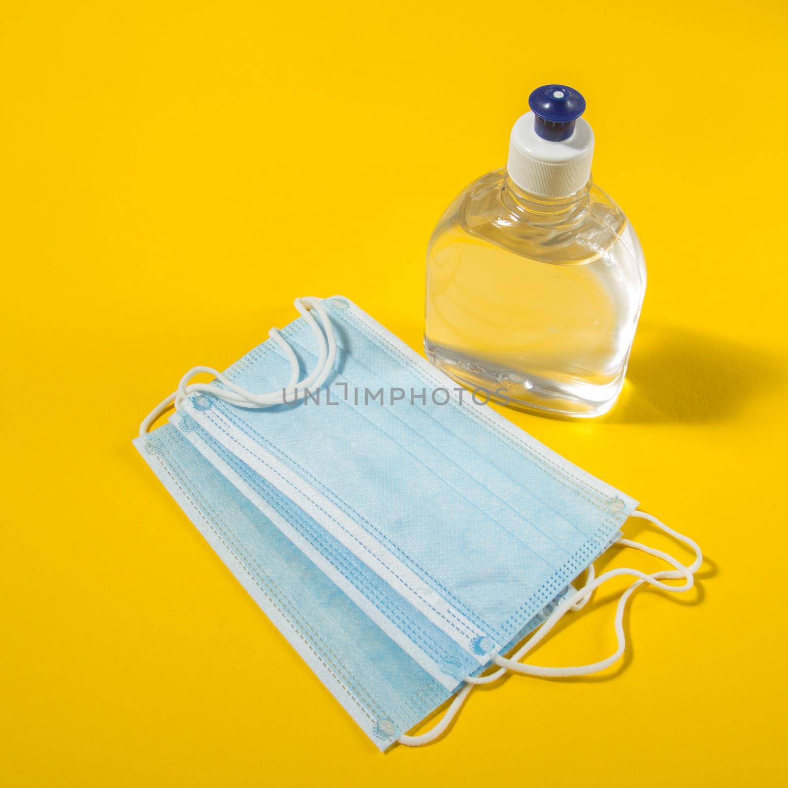 Alcohol gel hand sanitizer and disposable hygienic mask on yellow background