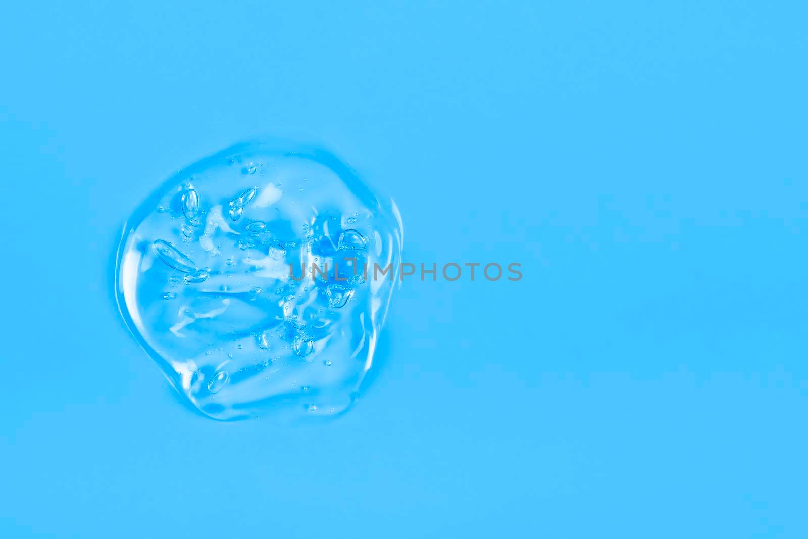 Clear transparent liquid gel drop or smear isolated on blue background. Top view. Virus protection or cosmetics concept. Serum texture. Banner with copy space.