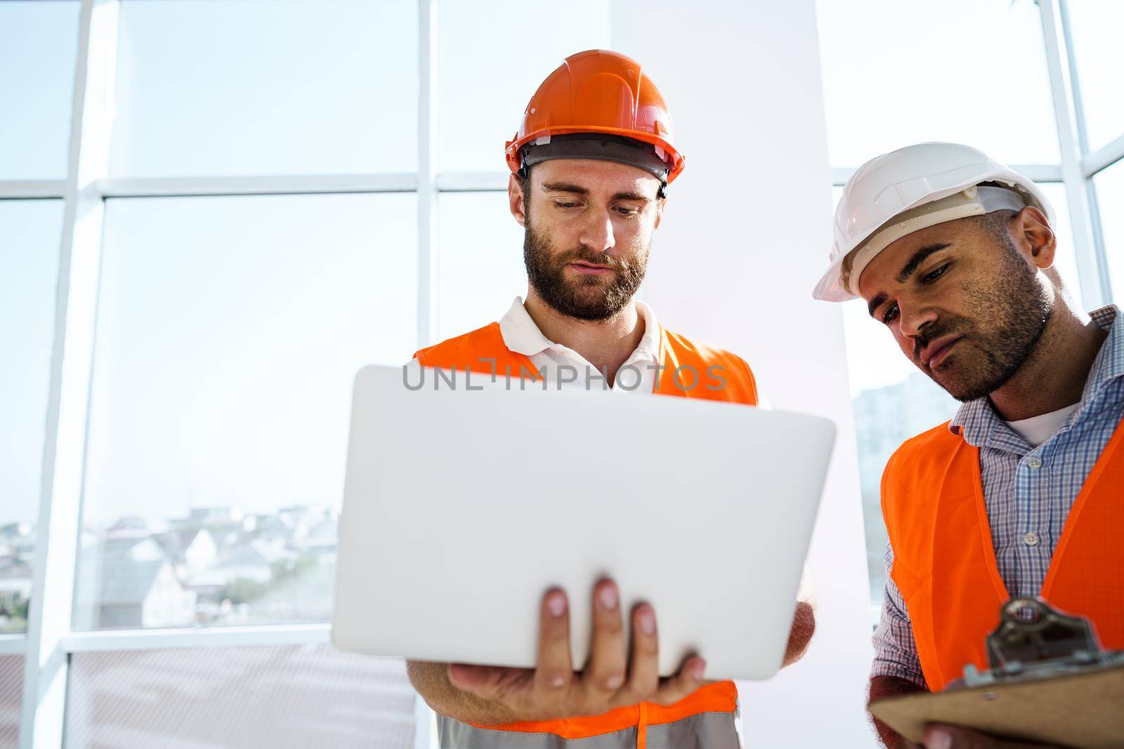 Two specialists supervisors in hardhats using laptop at construction site for work, close up