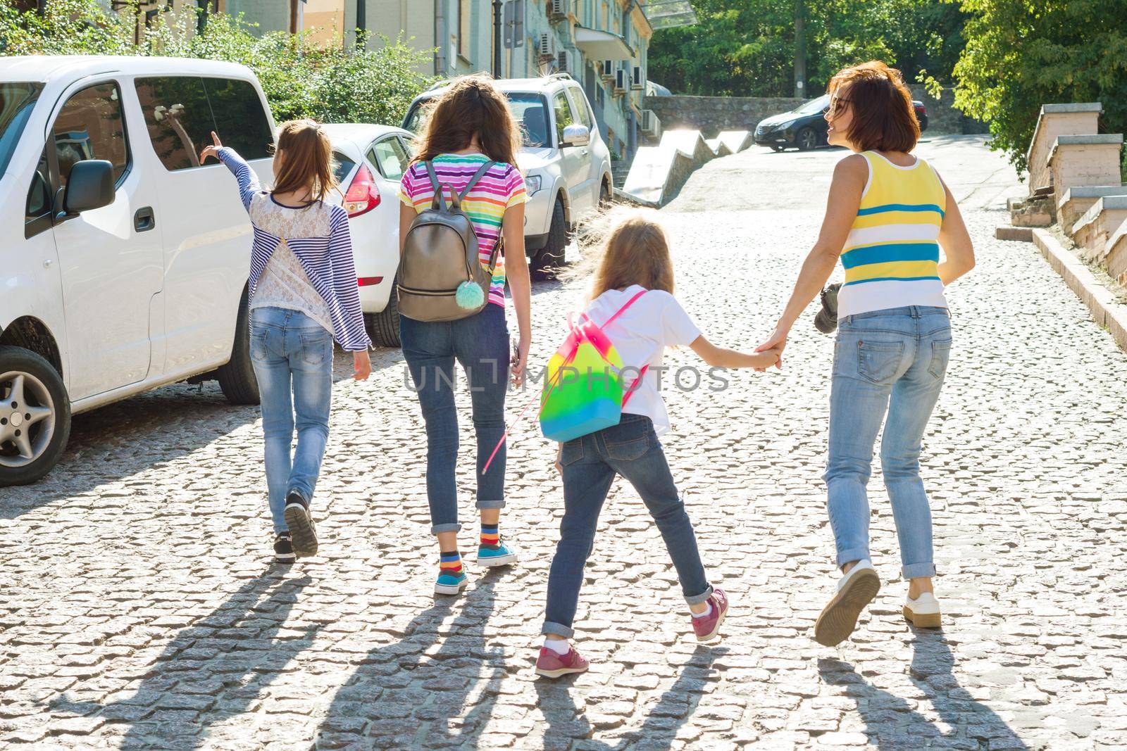 Mom and children holding hands walking around the city. Woman taking pictures at the camera, family tourism. by VH-studio
