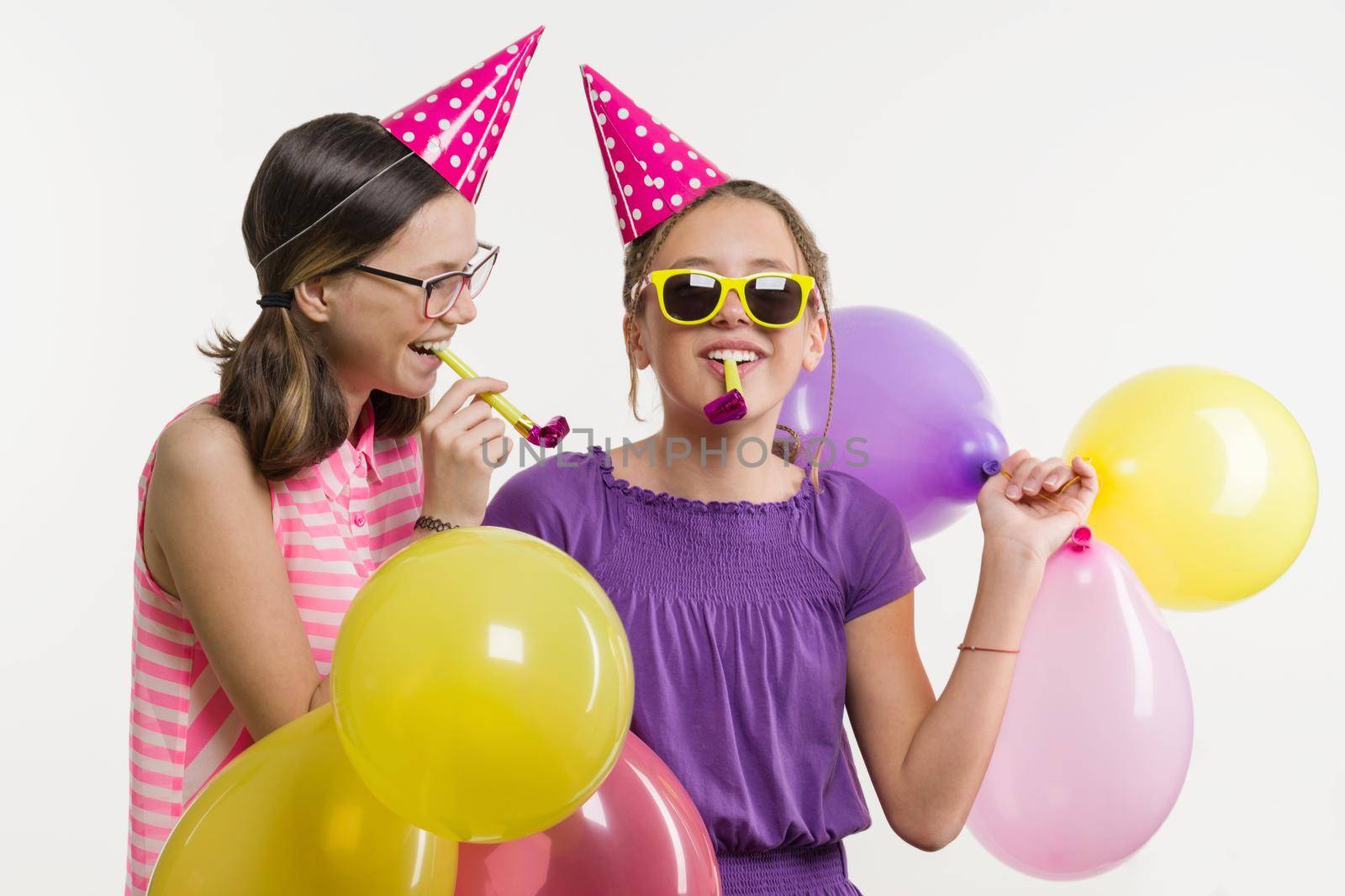 Teen girls at a party. Girls on a white background, in festive hats, blowing in the pipes