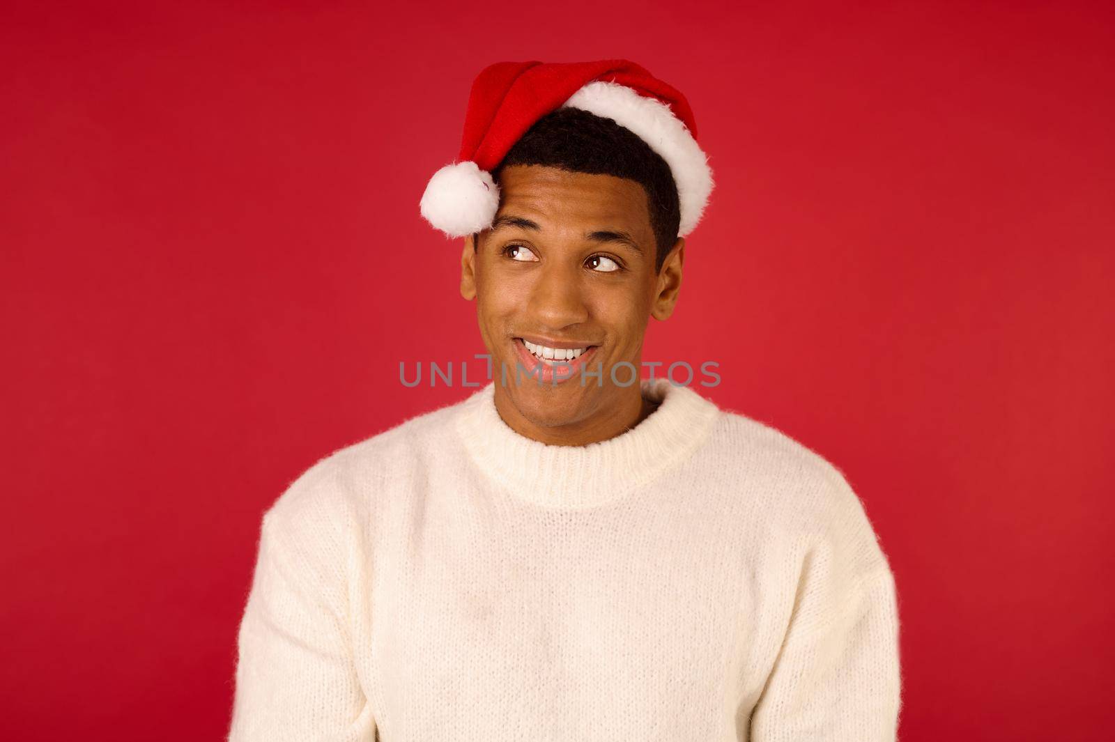 Christmas spirit. Young smiling guy in a white sweater and santa hat