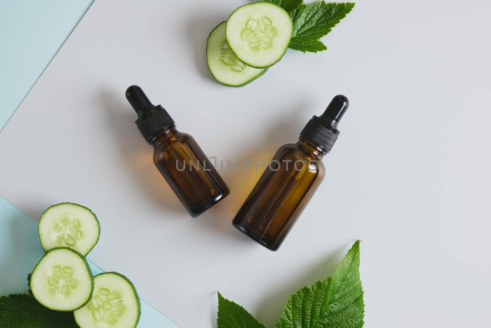 mock up blank amber glass bottle with pipettes and cucumber slices, dark brown dropper bottle with cosmetic product oil or serum with cucumber extract, gray-blue background copy space top view