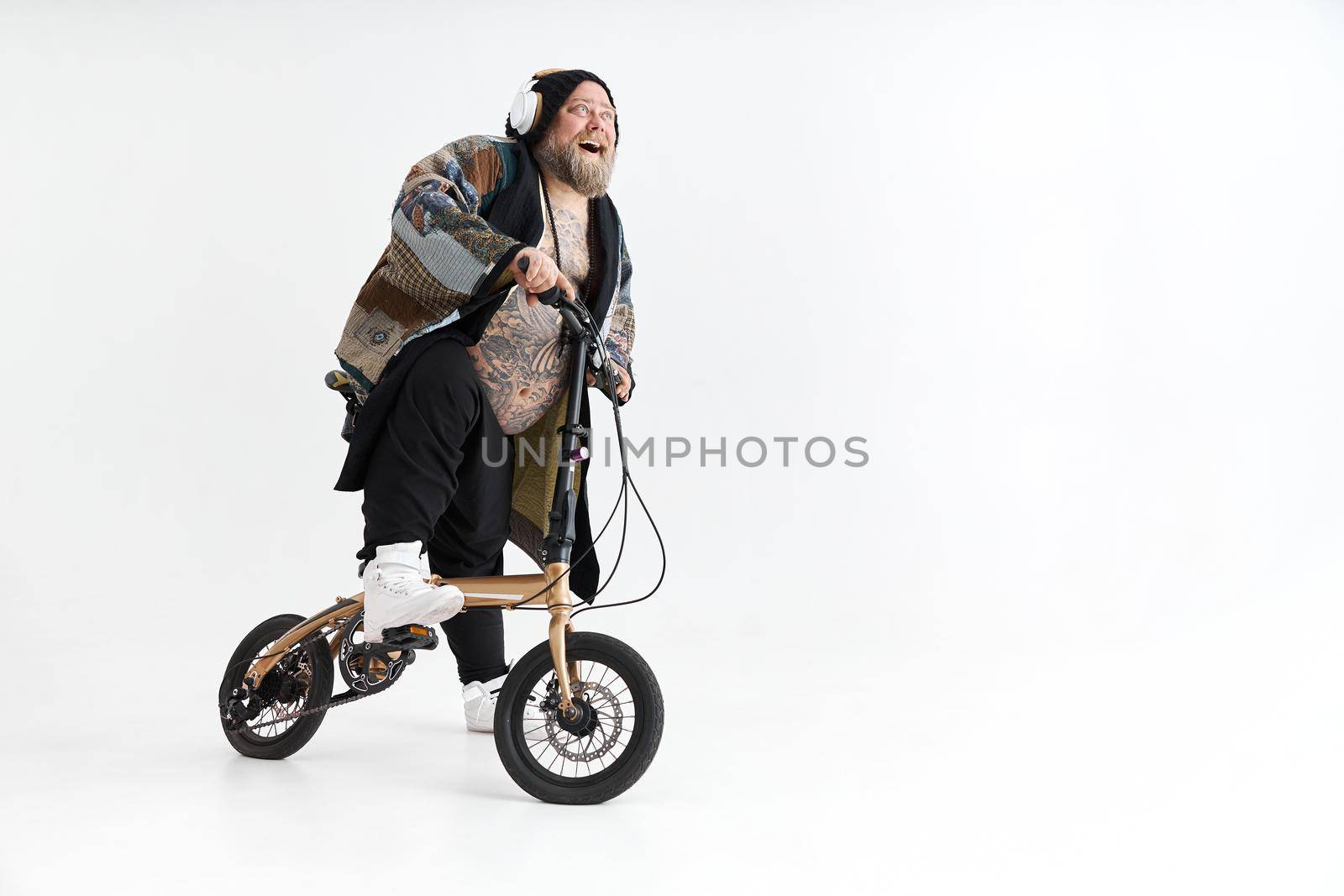 Big fat tattoed caucasian man in kimono is holding little bicycle and smilling by Yaroslav_astakhov