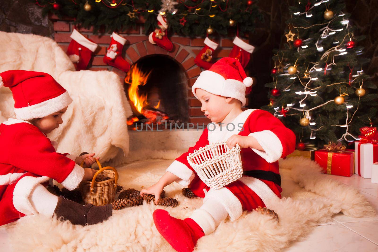 Children are sitting near fireplace and play with cones - Christmas decorations