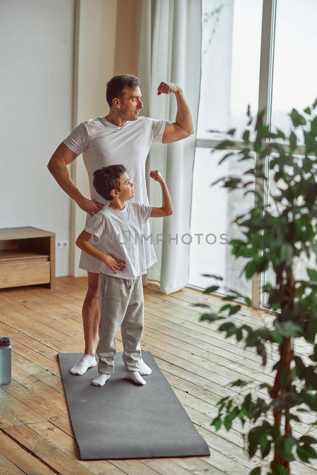 Sporty father and son demonstrating muscles indoors by Yaroslav_astakhov