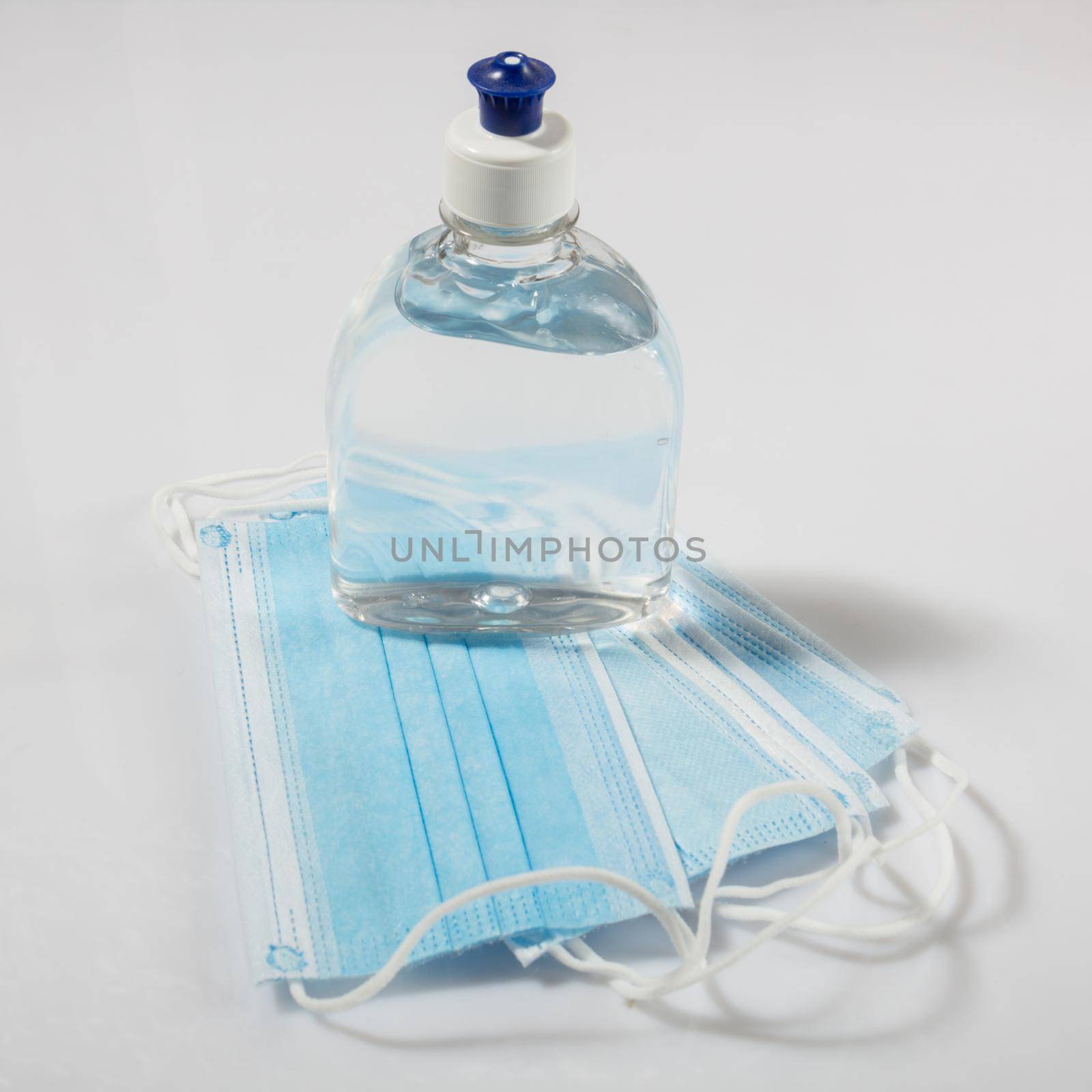 Alcohol gel hand sanitizer and disposable hygienic mask on gray background