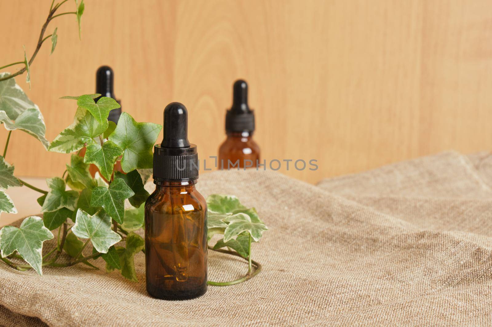 Brown glass bottle dropper with cosmetic oil and plant on linen fabric, brown background