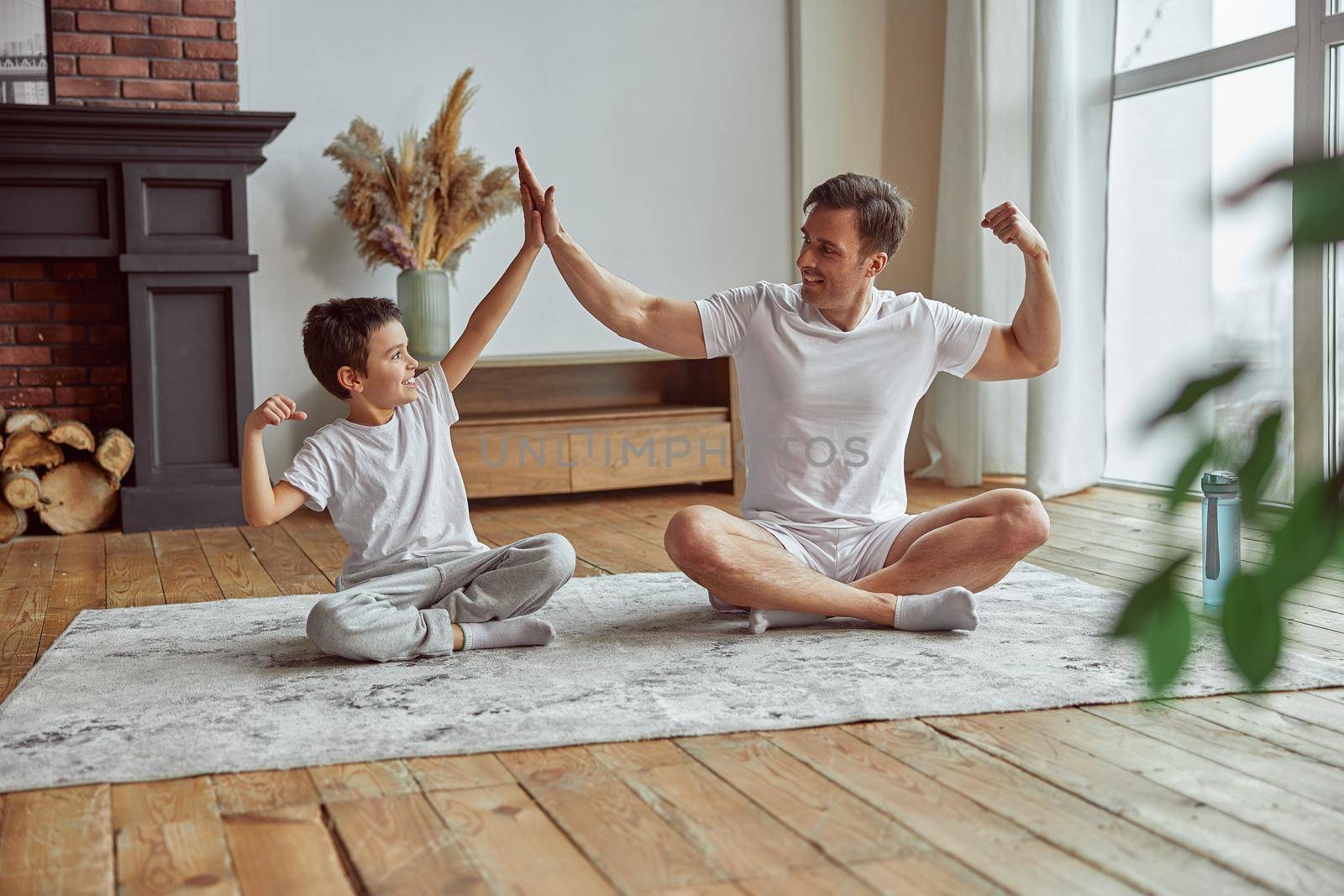 Happy sporty boy is training with dad together on mat at home and they are motivating each other