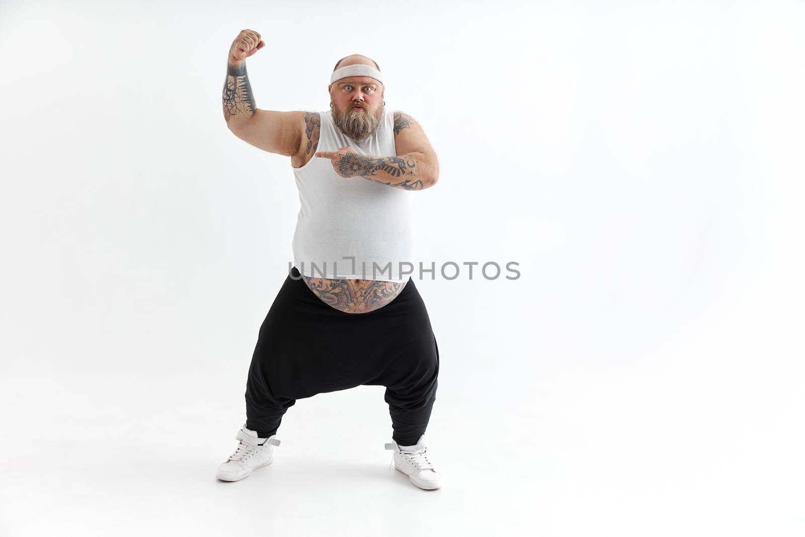 Happy fat man with big belly and tattoes in sports wear posing on white background