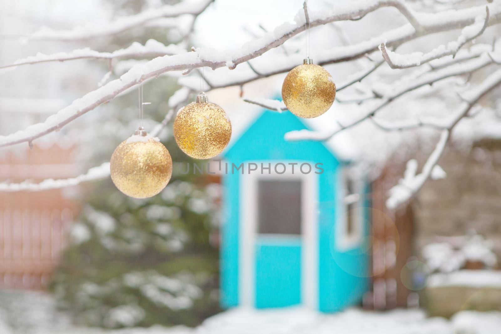 golden christmas tree balls on tree branches and winter snow. Christmas balls near fur-trees covered with a snow and small wooden house. Playground for children at backyard