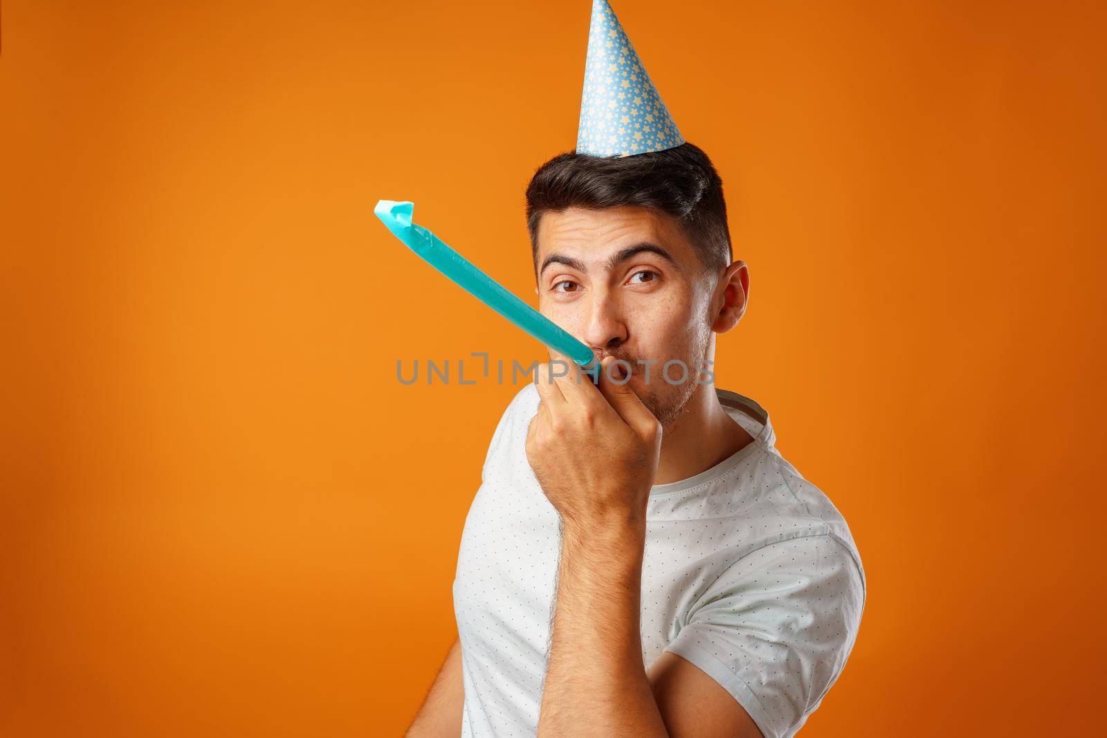 Happy man with party cone blowing into party horn against yellow background