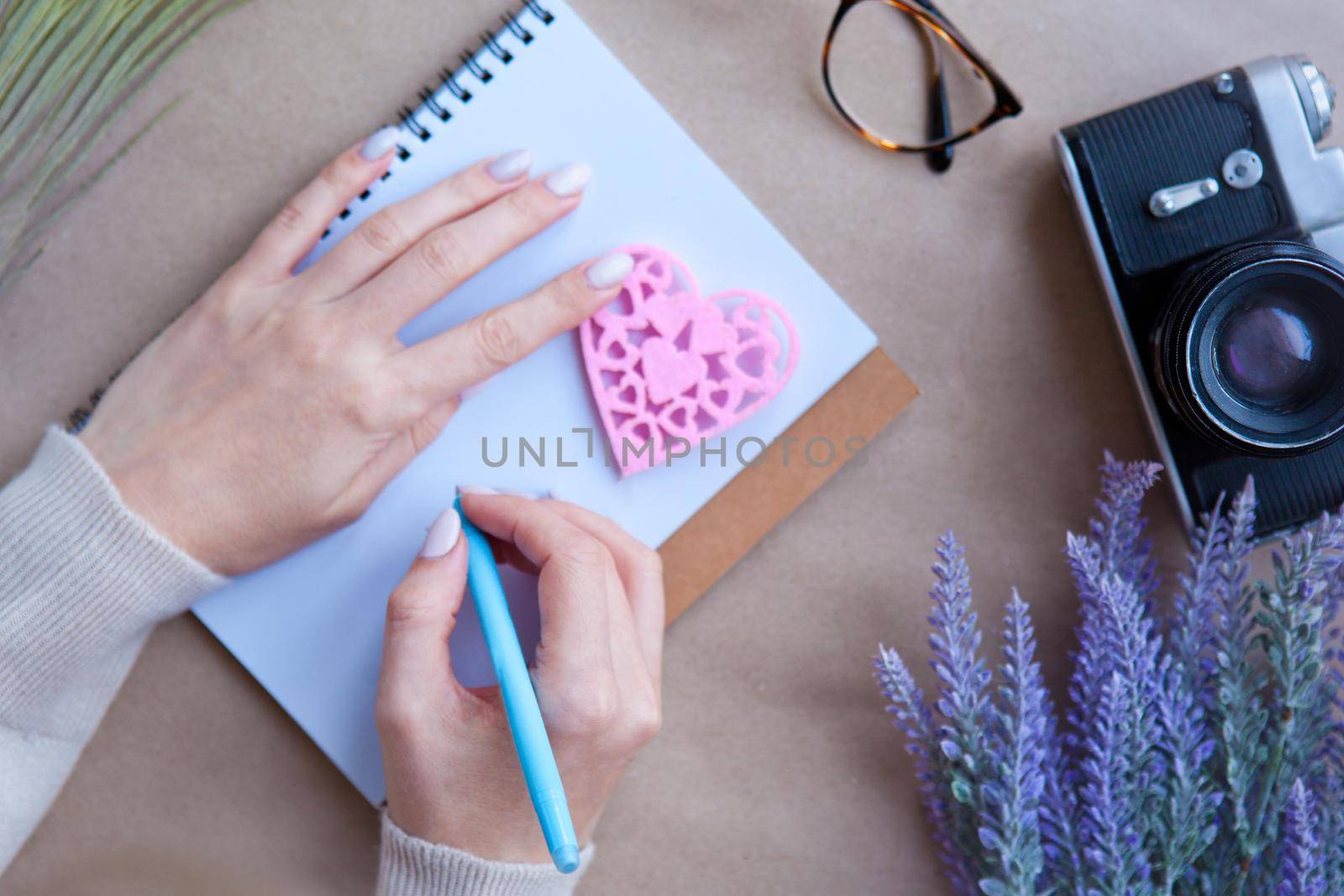 Wooden heart LOVE and woman hands behind notebook on the table and retro camera. Letter writting concept. Heart shape symbol. Valentines - romantic greeting and letters lifestyle feelings concept