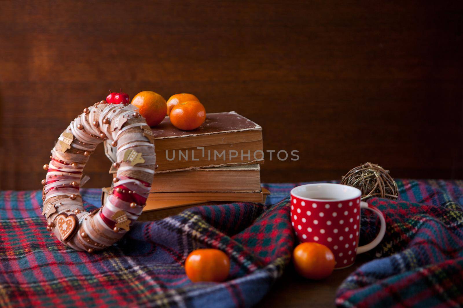 Red dotted Mug or tea cup with hot chocolate on a Scottish blanket. Cozy home concept with books. Cup of hot chocolate. Traditional homemade Christmas cocoa and mandarin orange Citrus and wreath