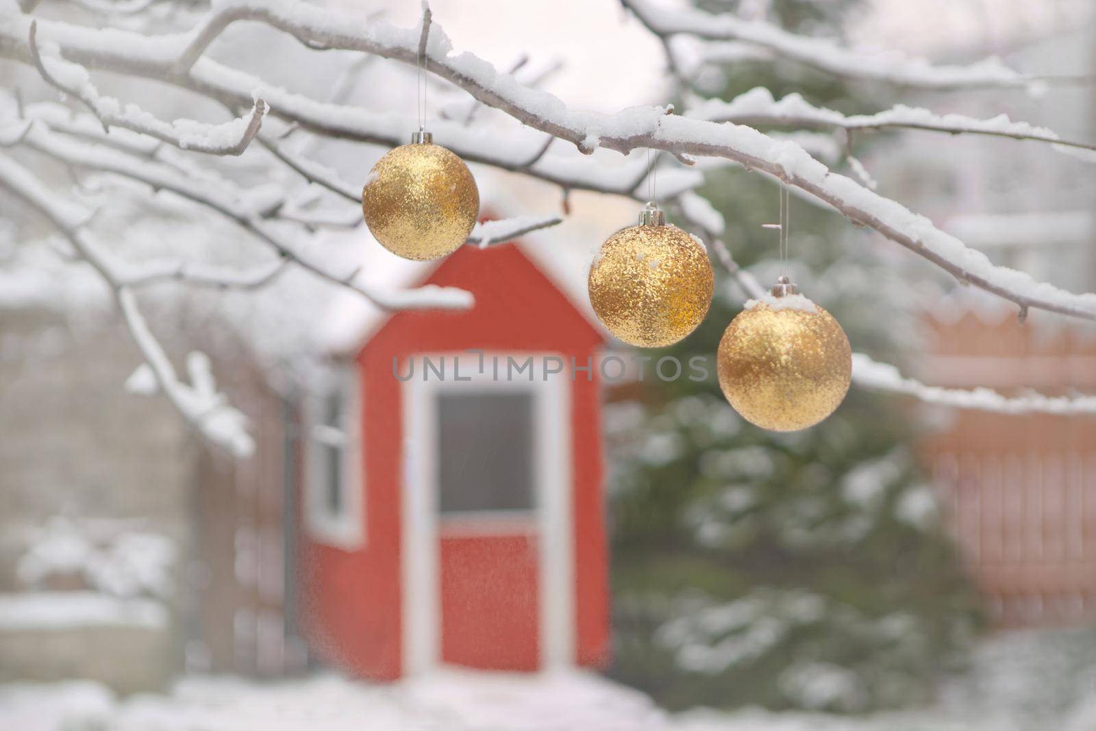 golden christmas tree balls on tree branches and winter snow. Christmas balls near fur-trees covered with a snow and small red wooden house.