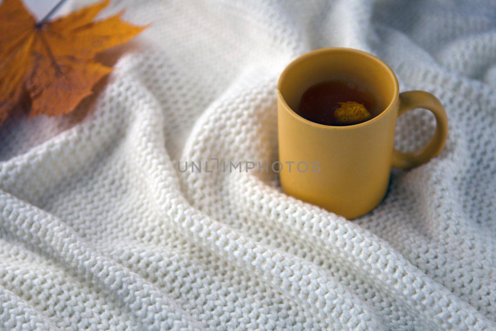 yellow tea cup with white scarf background, ceramic cup with autumn leaf, white blanket with hot drink in a mug