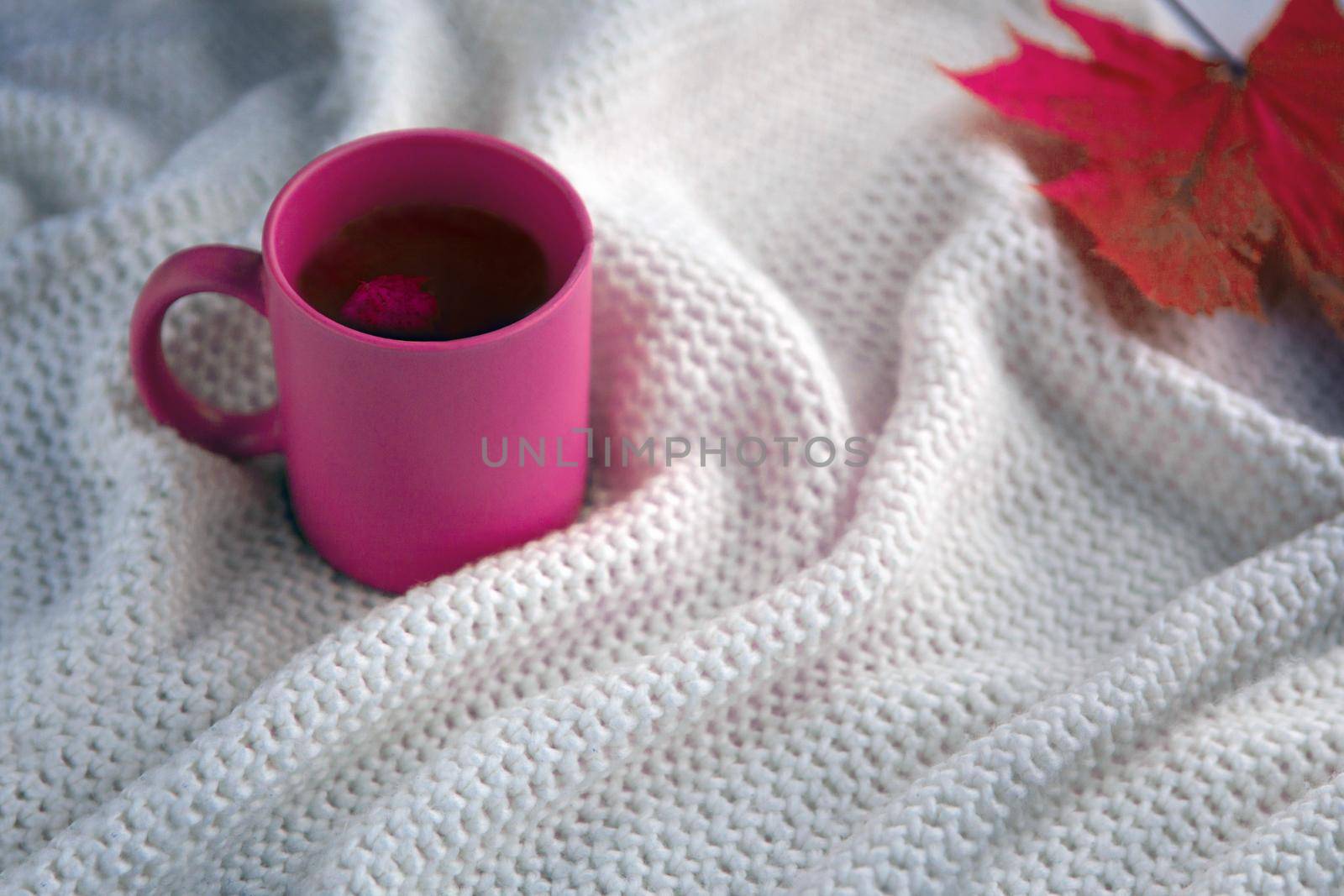 pink tea cup with white scarf background, ceramic cup with autumn leaf, white blanket with hot drink in a mug