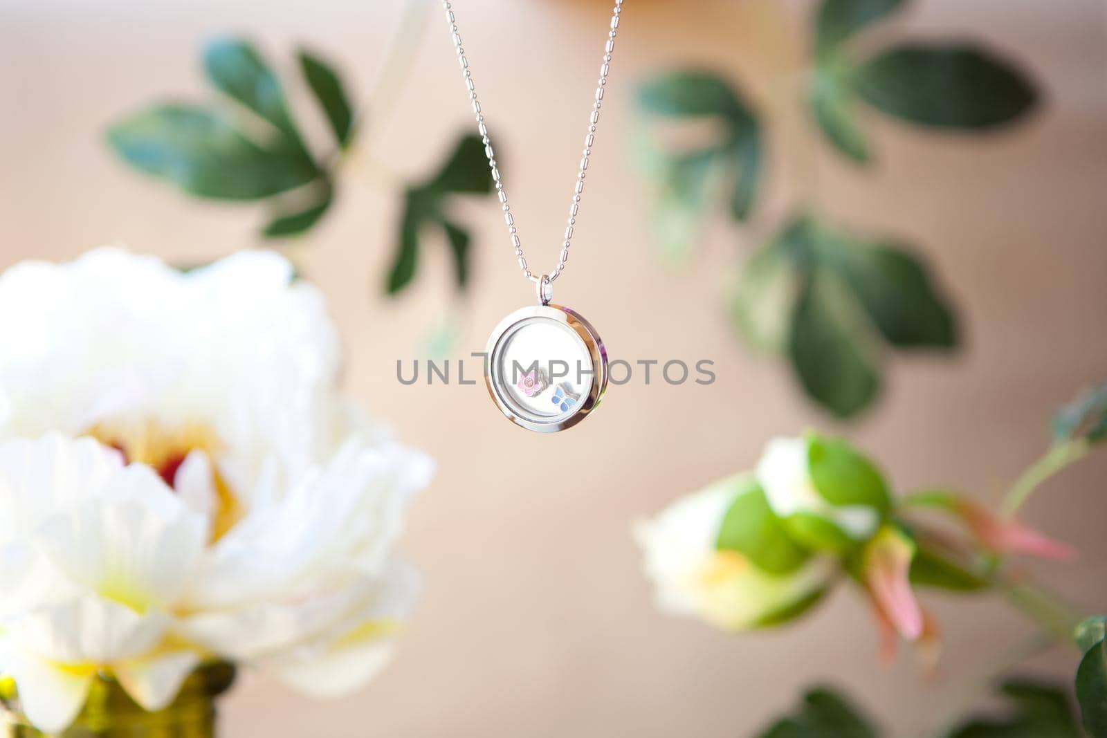 shining Silver necklace for lady on peonies flower background. Luxury silver jewelry chains with glass. Beautiful precious metal present for woman on brown. Luxury jewelry gift with floral background