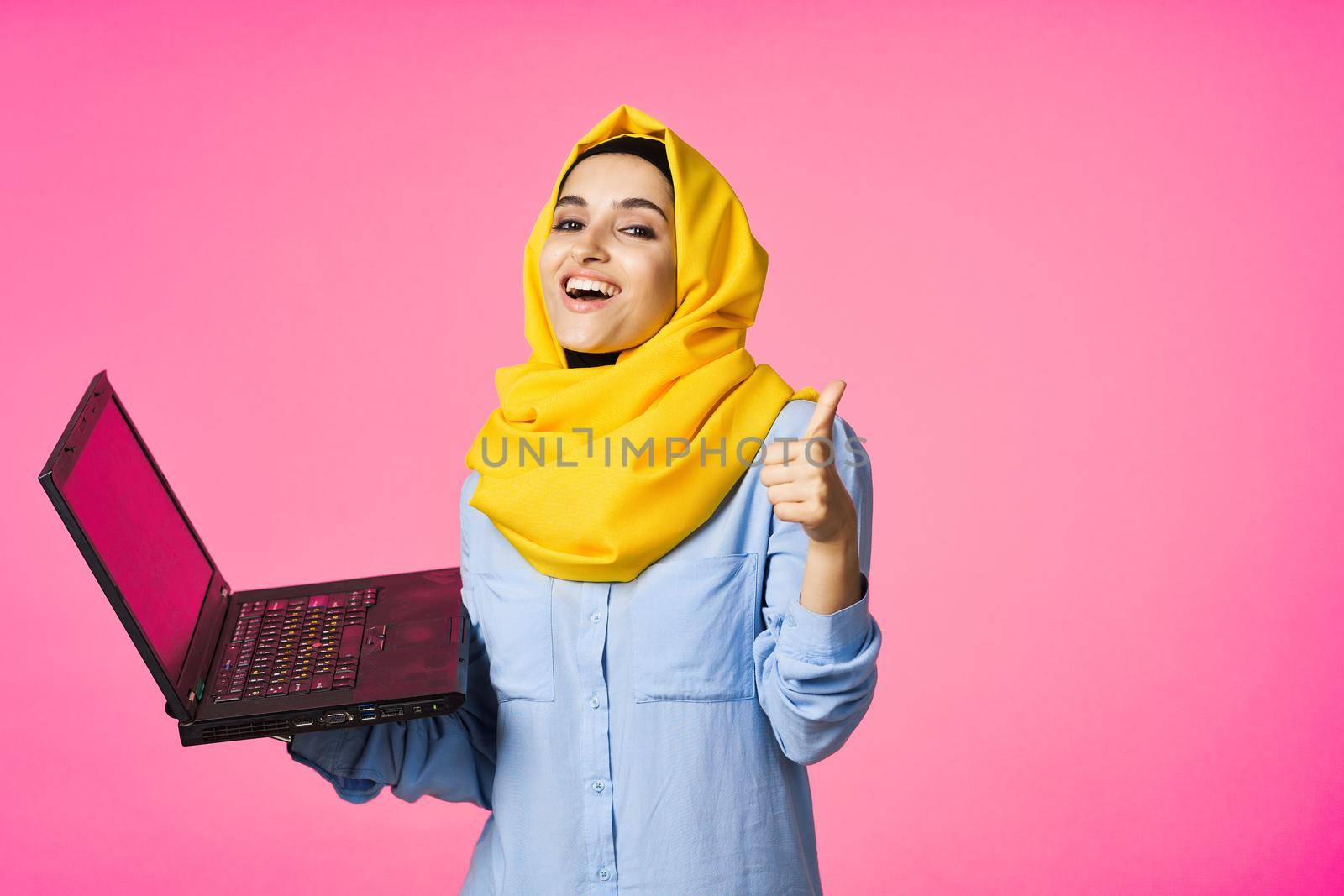 muslim woman in yellow hijab with laptop technology student pink background by Vichizh