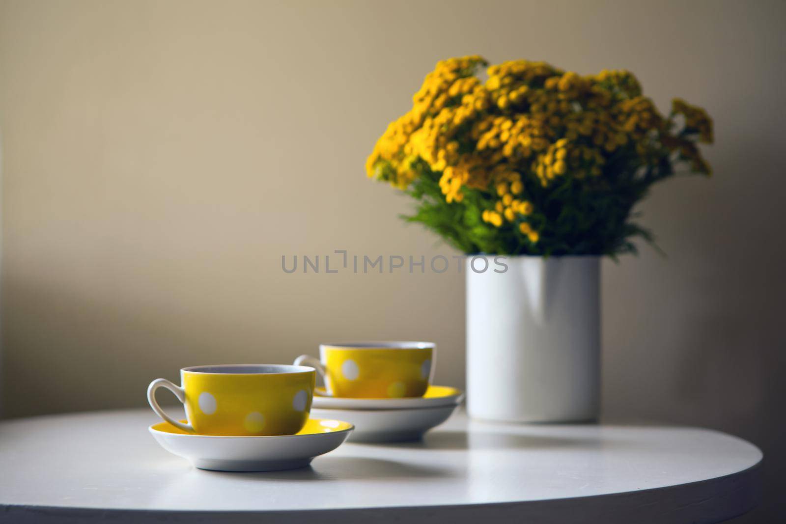 Yellow dotted retro cups and yellow chrysanthemum flowers on white table. Vintage teaset